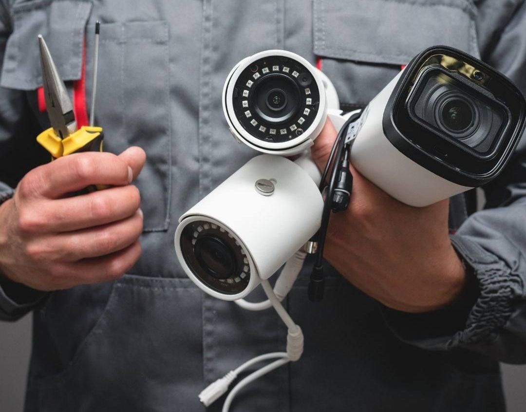 Security System Repair A man is holding two security cameras and a pair of pliers.
