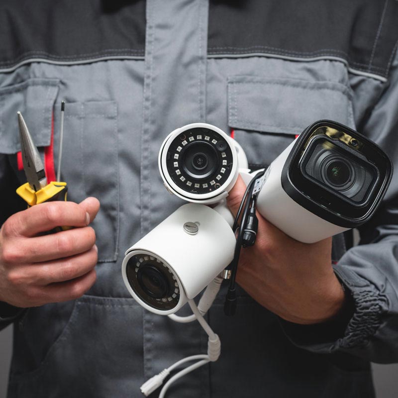 A man is holding two security cameras and a pair of pliers.
