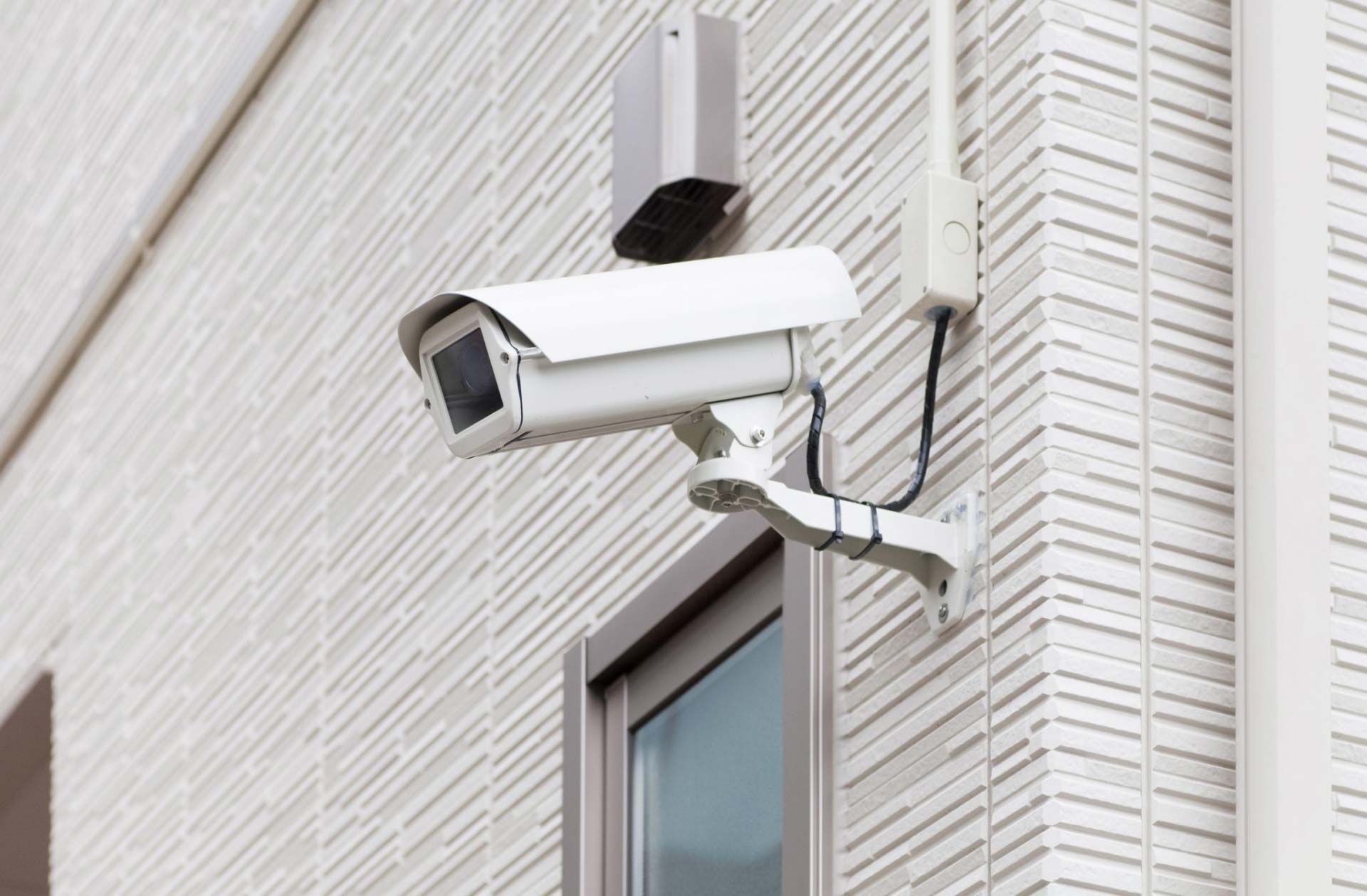 A security camera is mounted on the side of a building next to a window.