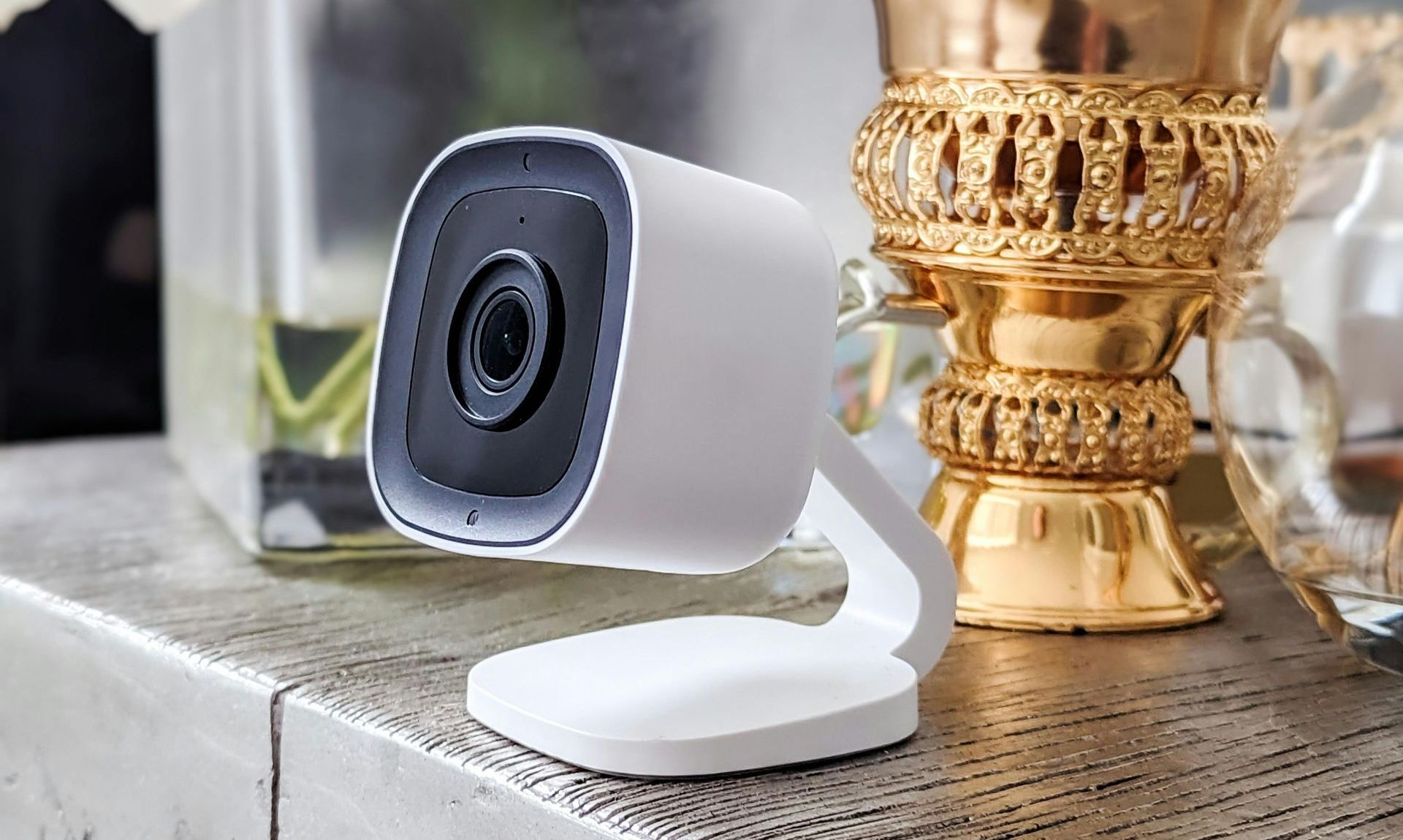 A security camera is sitting on a table next to a vase.