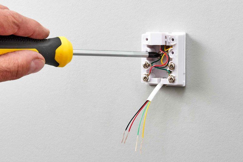 A person is using a screwdriver to fix an electrical box on a wall.