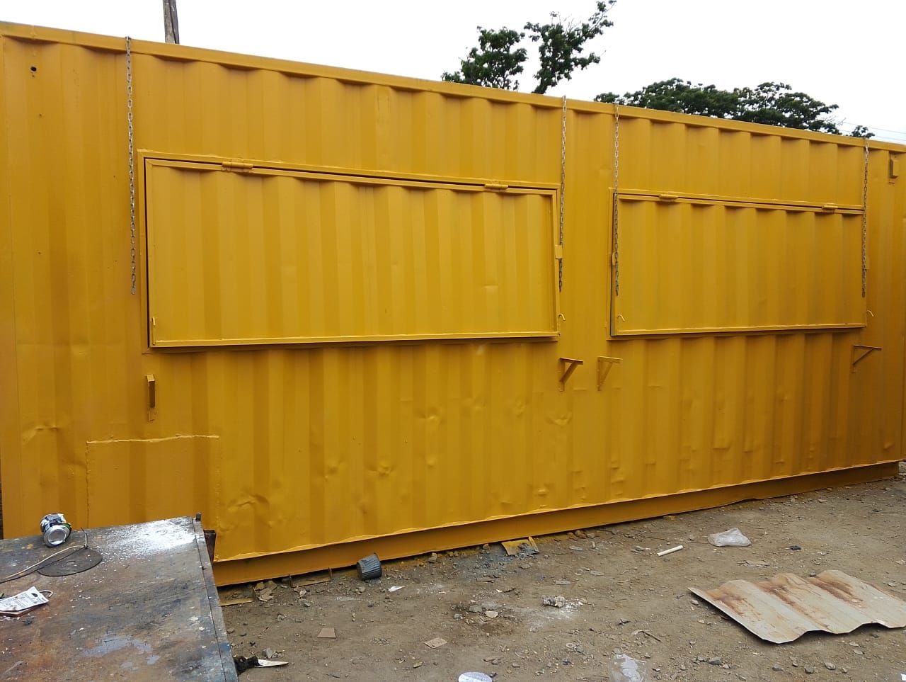 Un contenedor de transporte amarillo modificado con dos grandes ventanas de servicio horizontales en uno de sus laterales.