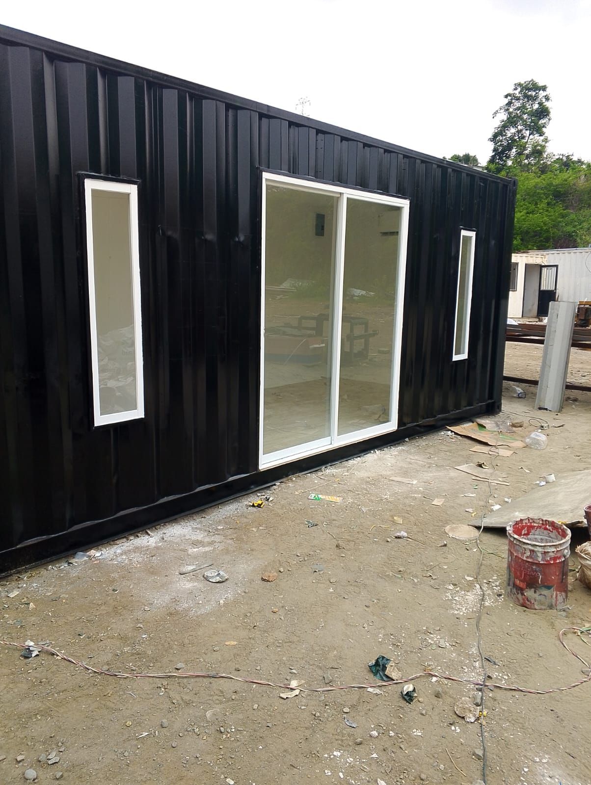 Un contenedor de transporte de metal negro reconvertido en oficina o estudio, con una gran puerta corredera de cristal
