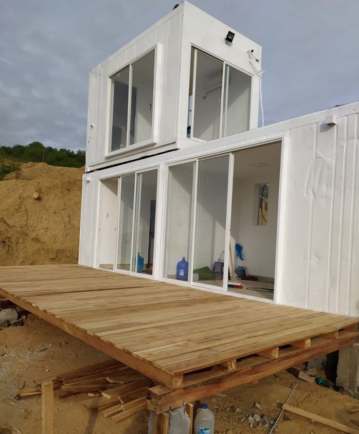 Una casa prefabricada blanca construida con contenedores de transporte, con una gran terraza de madera al frente