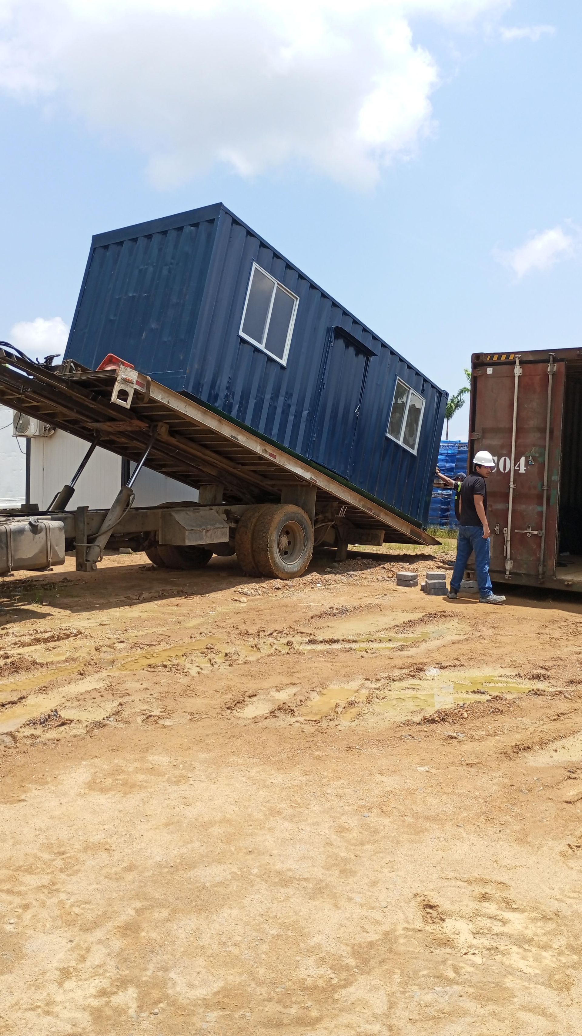 Un contenedor modular de oficina azul está siendo descargado de un camión de plataforma inclinado