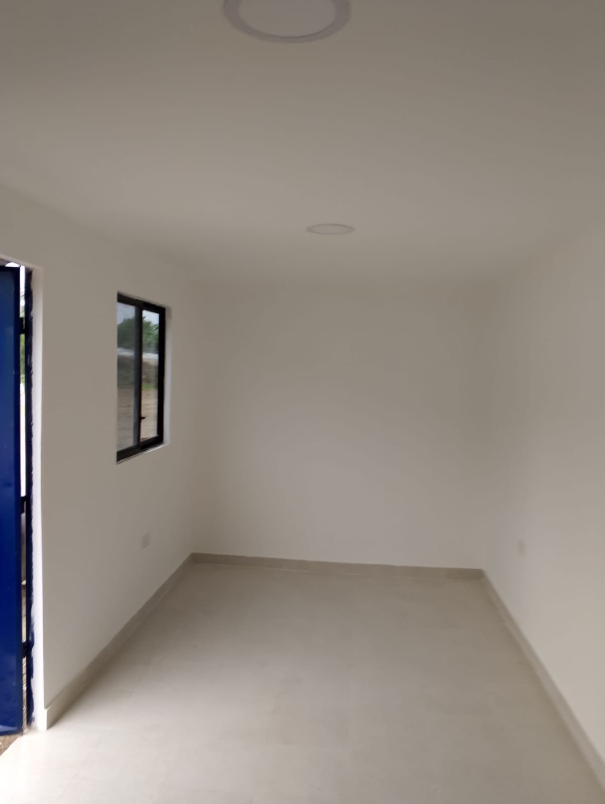 Una habitación rectangular vacía y muy iluminada, con paredes blancas, suelo claro, una ventana