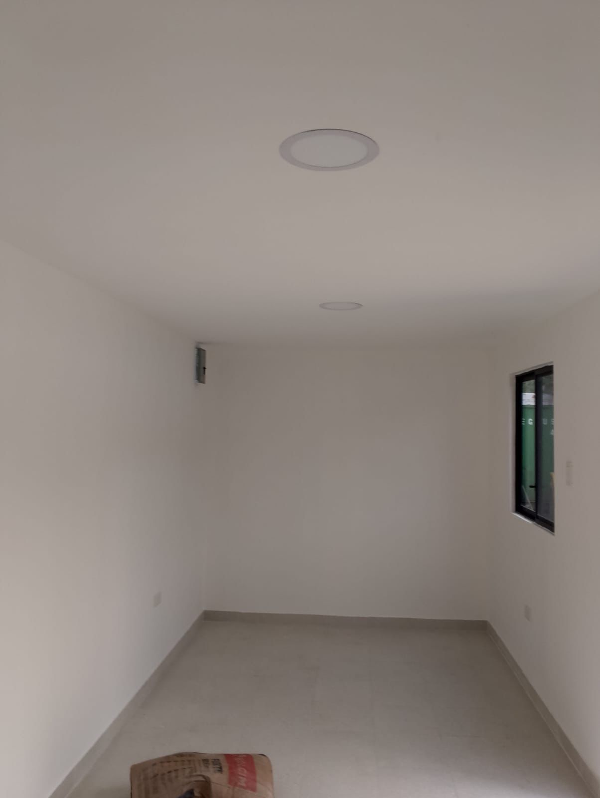 Una habitación pequeña y vacía con paredes blancas, suelo de baldosas, una sola ventana en la pared derecha
