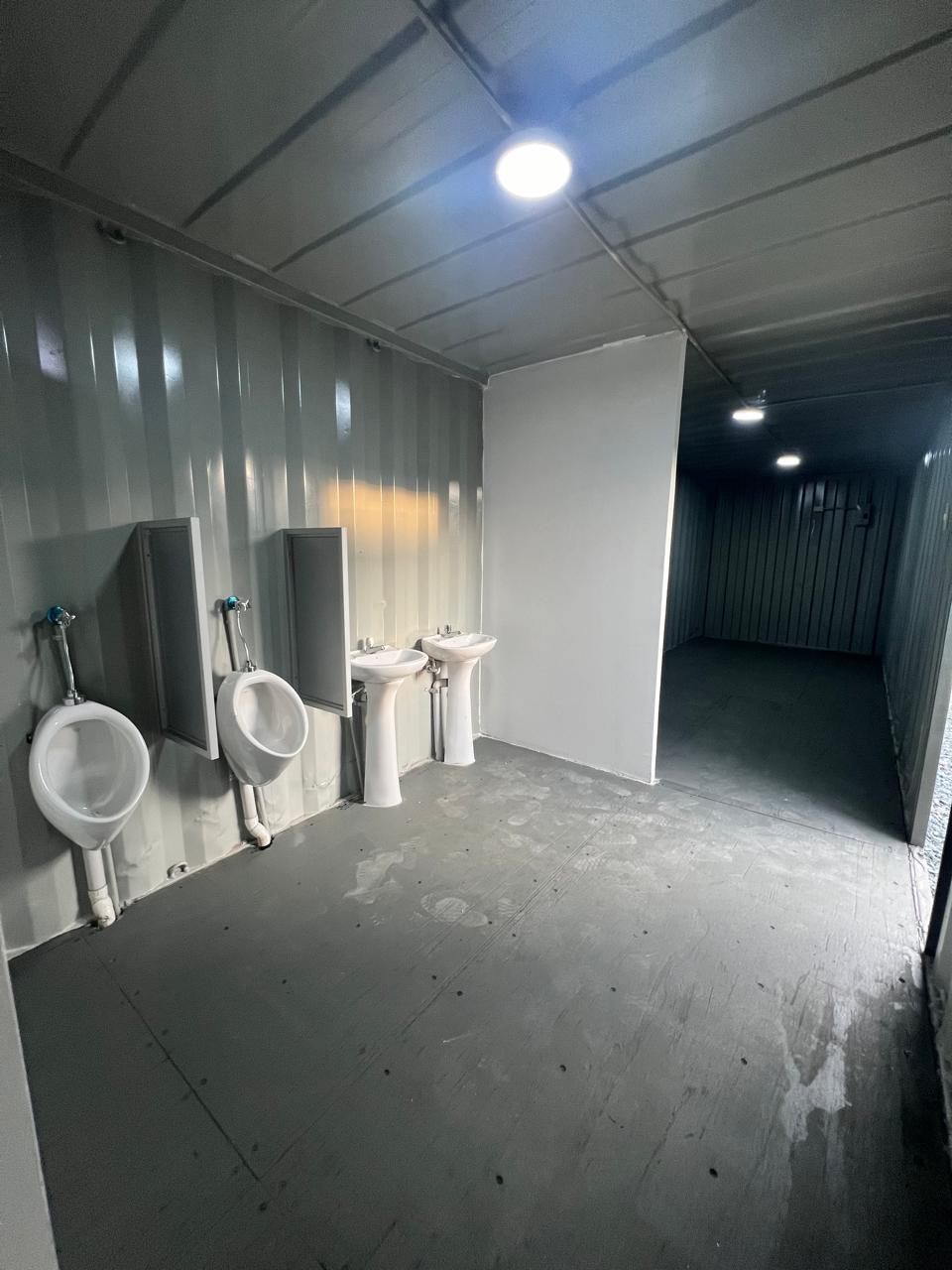 El interior de un moderno baño público cuenta con dos urinarios blancos separados por mamparas