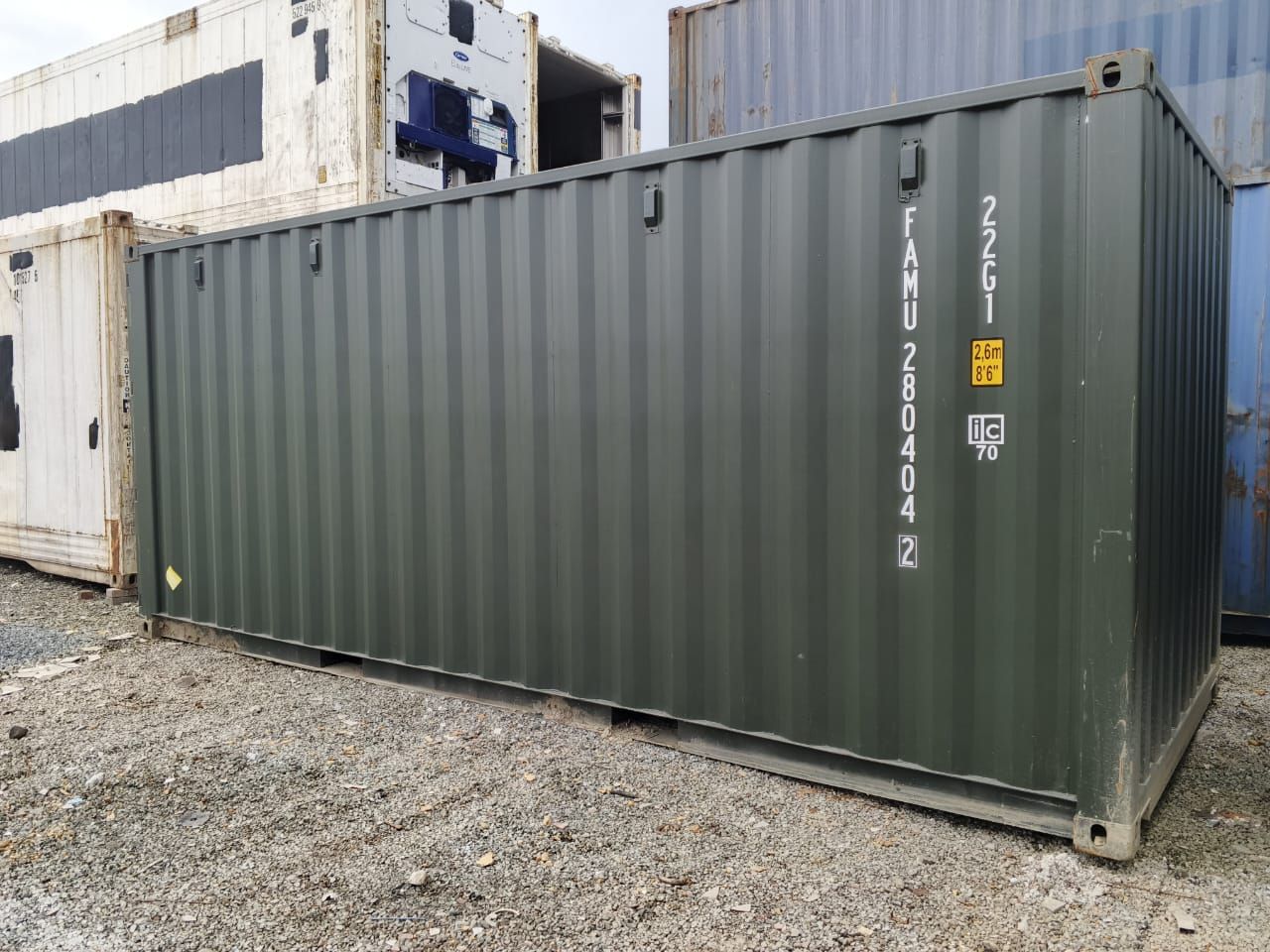 Un sencillo contenedor de transporte de color verde oliva oscuro se encuentra sobre un terreno de grava