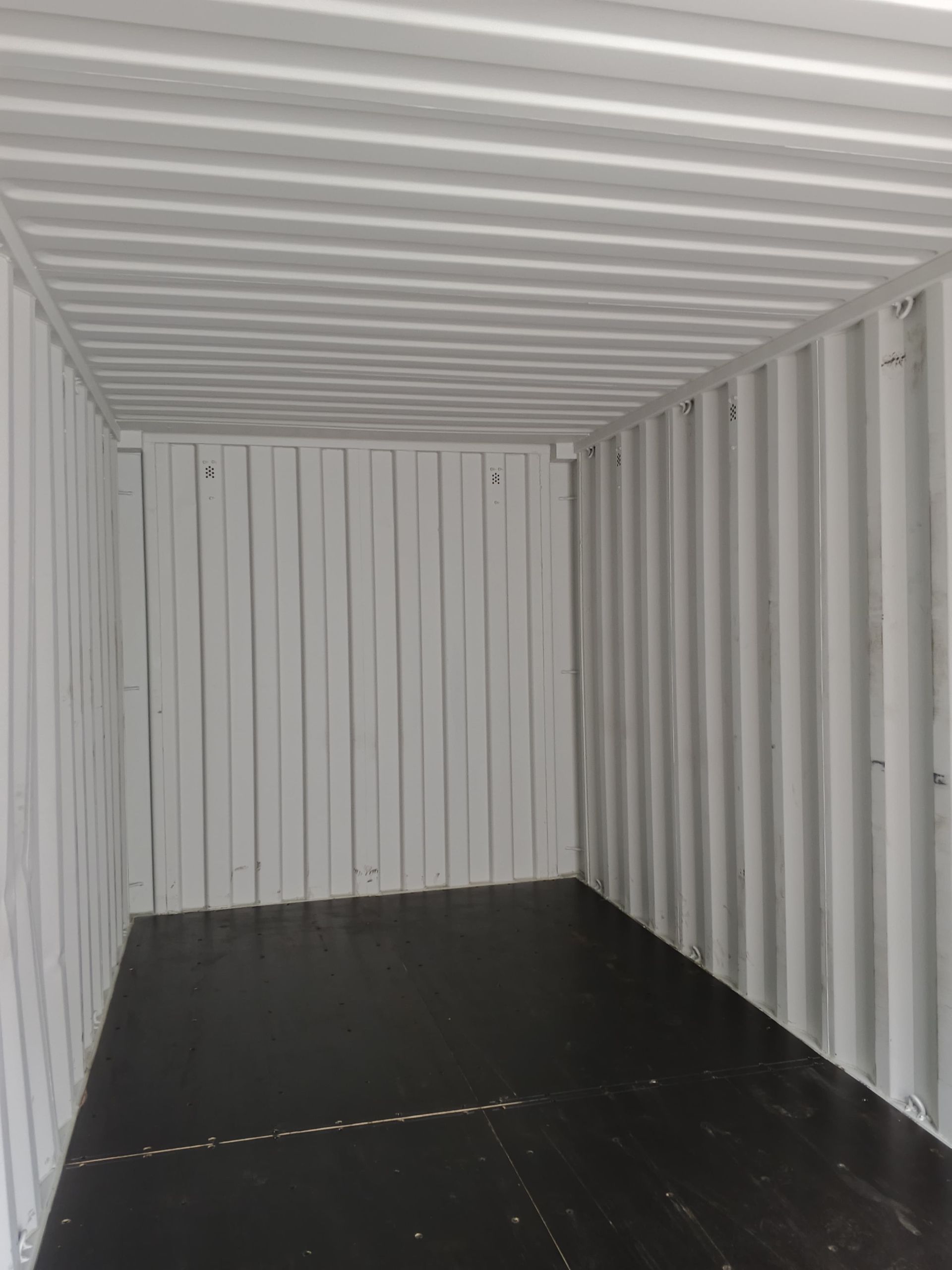 El interior de un contenedor de transporte vacío con paredes blancas corrugadas y un suelo oscuro.