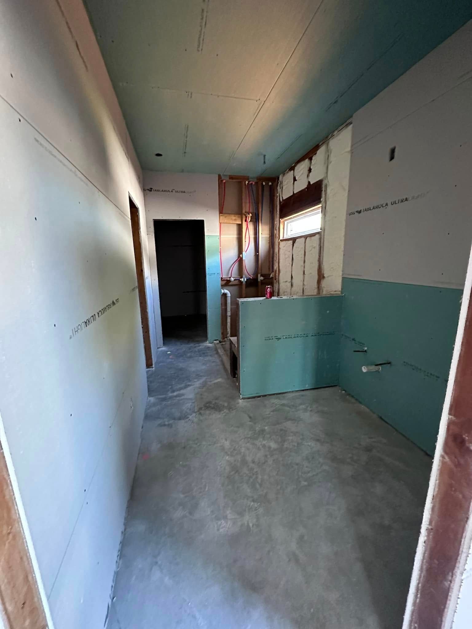 Narrow unfinished hallway with peeling white and turquoise walls, concrete floor, and a dark doorway at the end