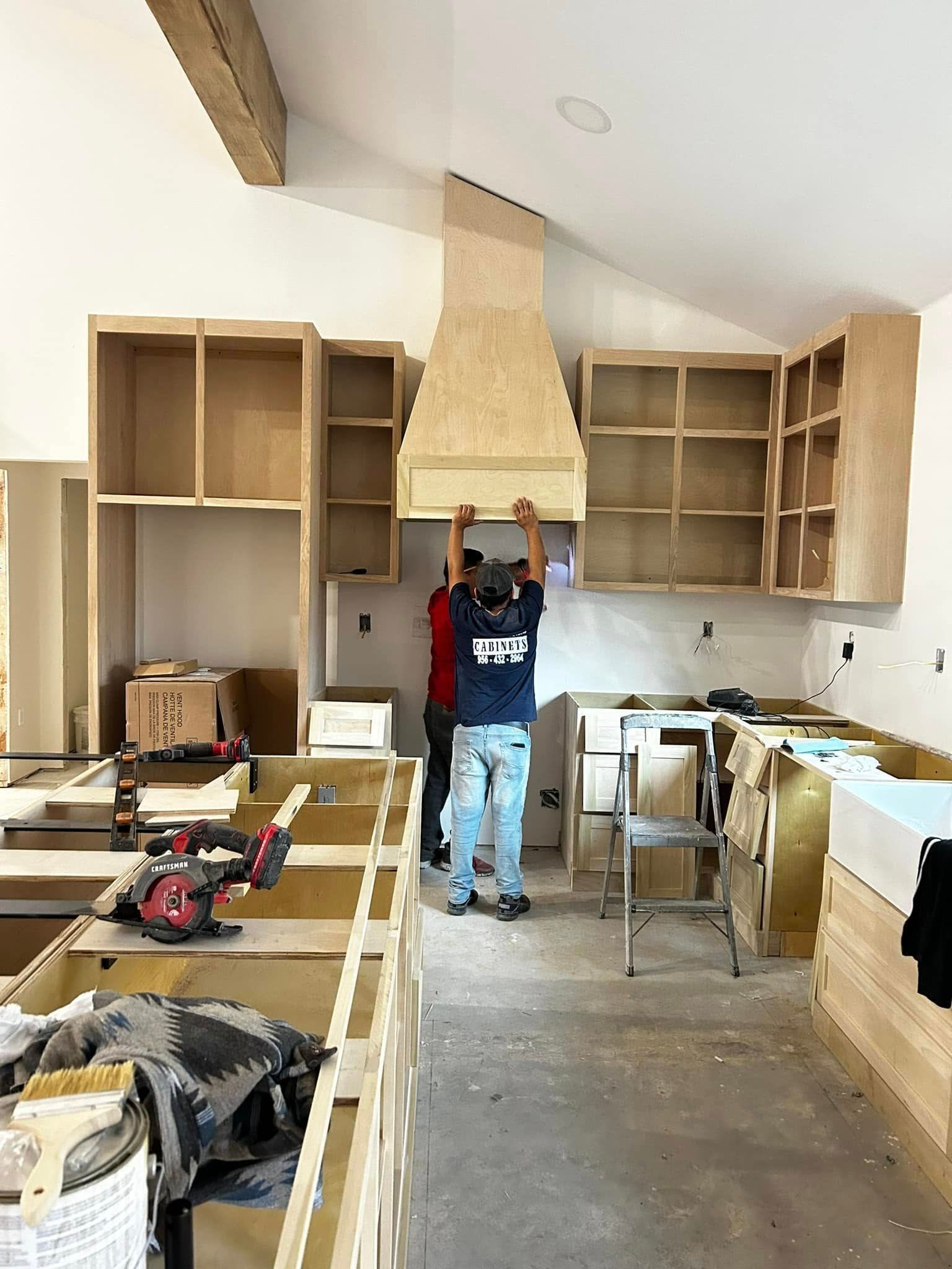Worker installing kitchen cabinets in an unfinished kitchen with tools and materials scattered around