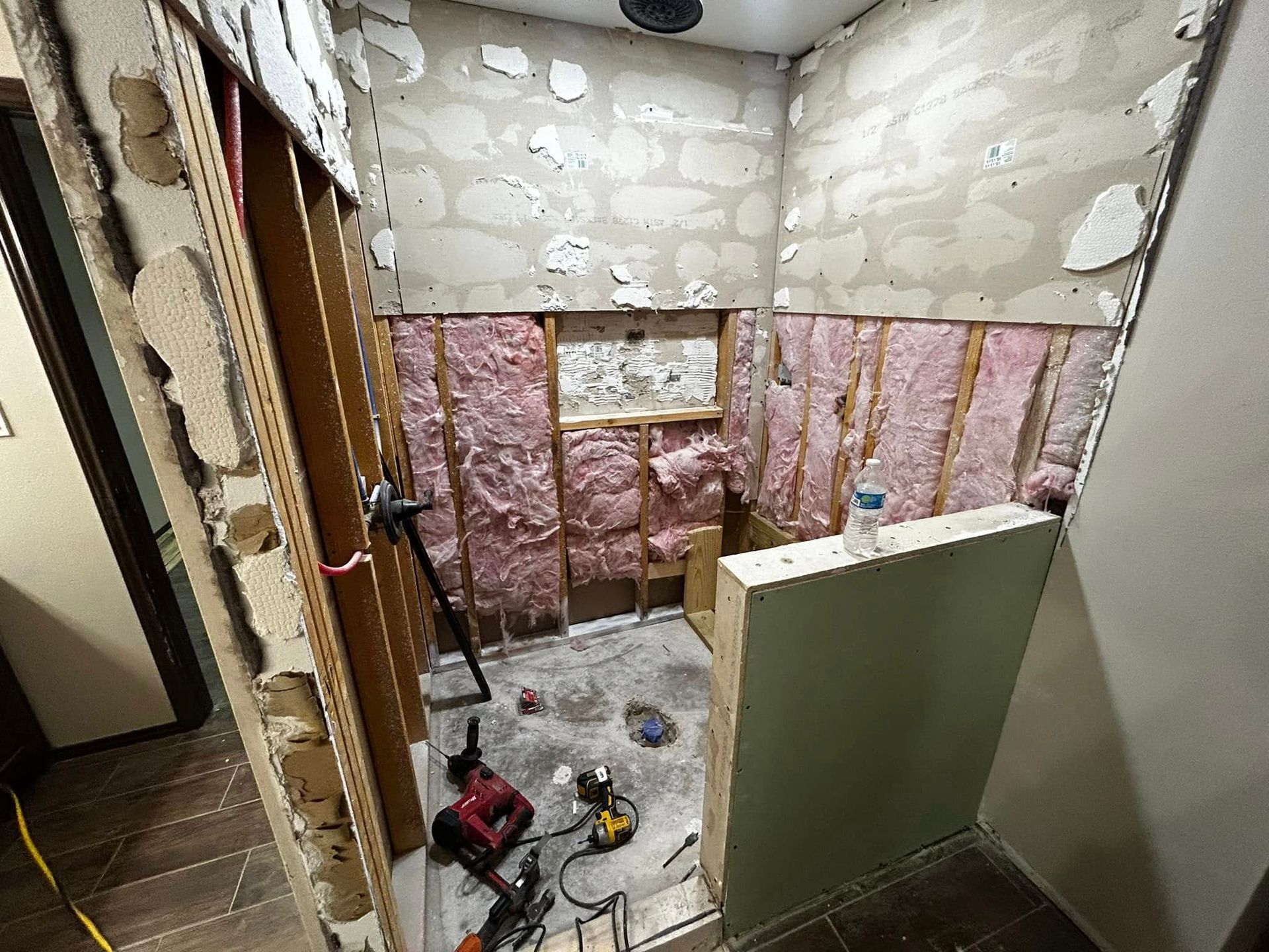 Partially renovated bathroom with exposed insulation, unfinished walls, and tools on the floor