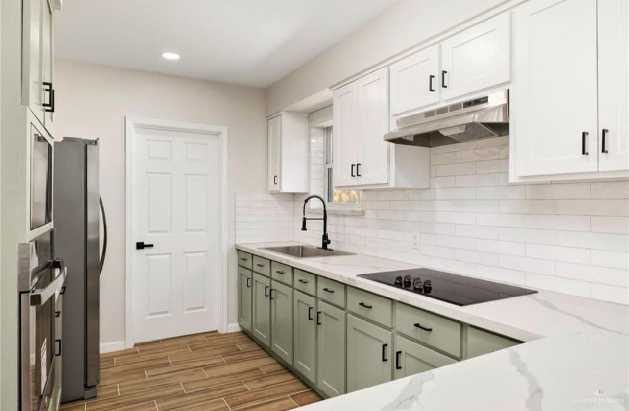 Bright white kitchen with sage cabinets, stainless appliances, subway tile backsplash, and wood floor