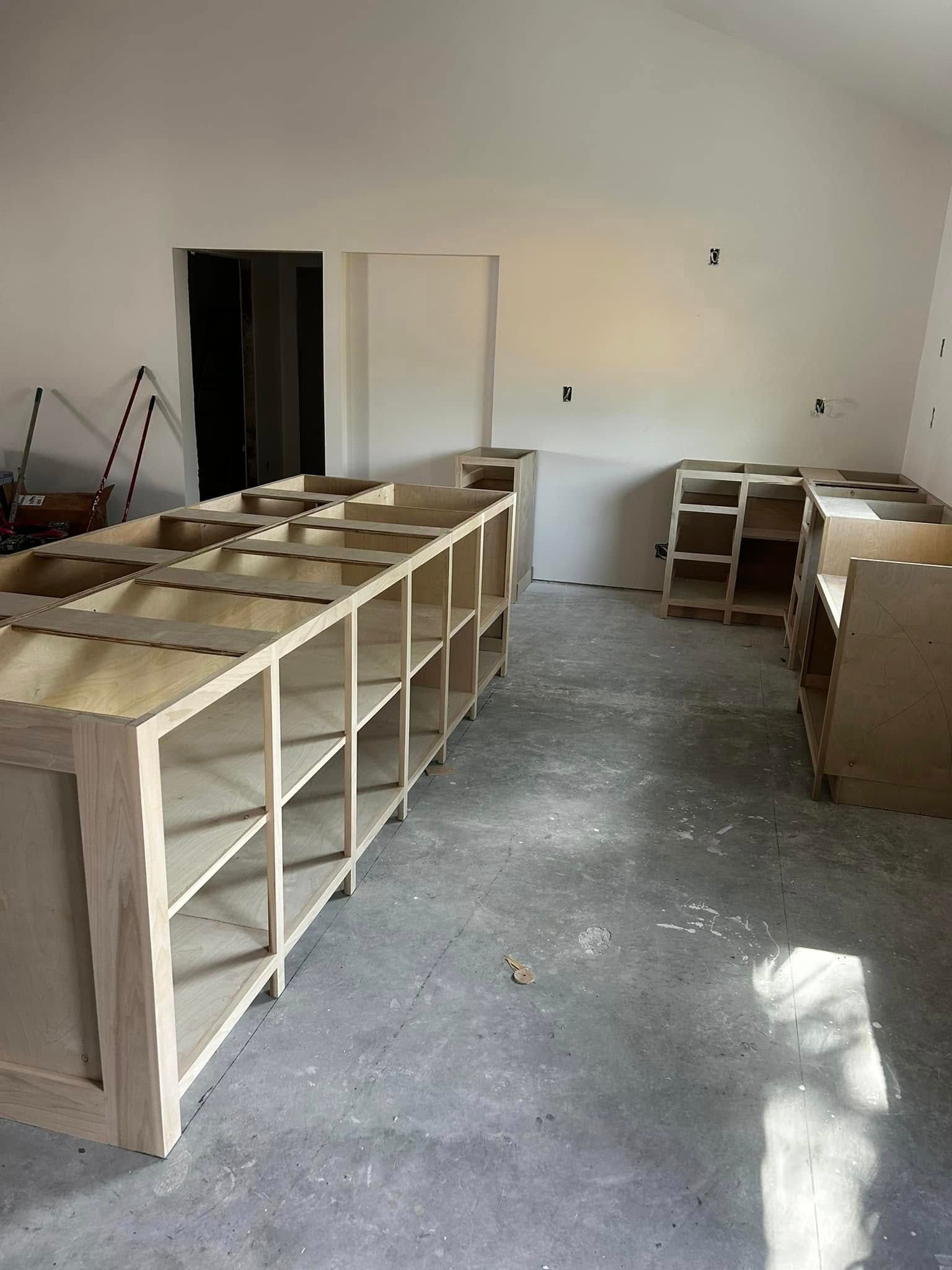 Empty room with unfinished wooden shelving and cabinets on a concrete floor
