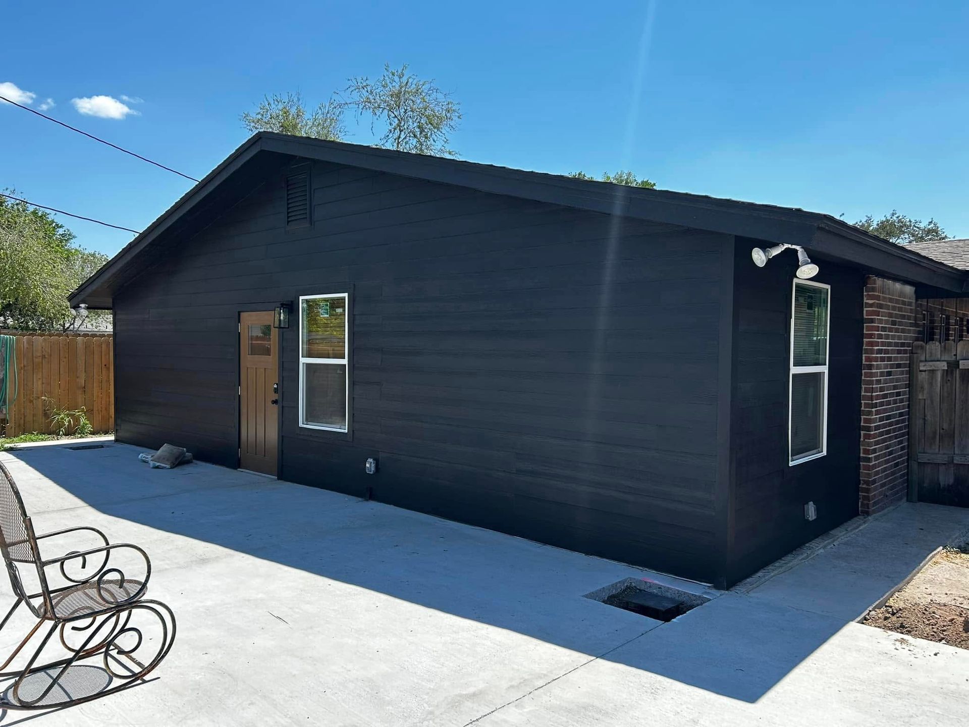 Black exterior building with a concrete driveway, small windows, and clear blue sky.