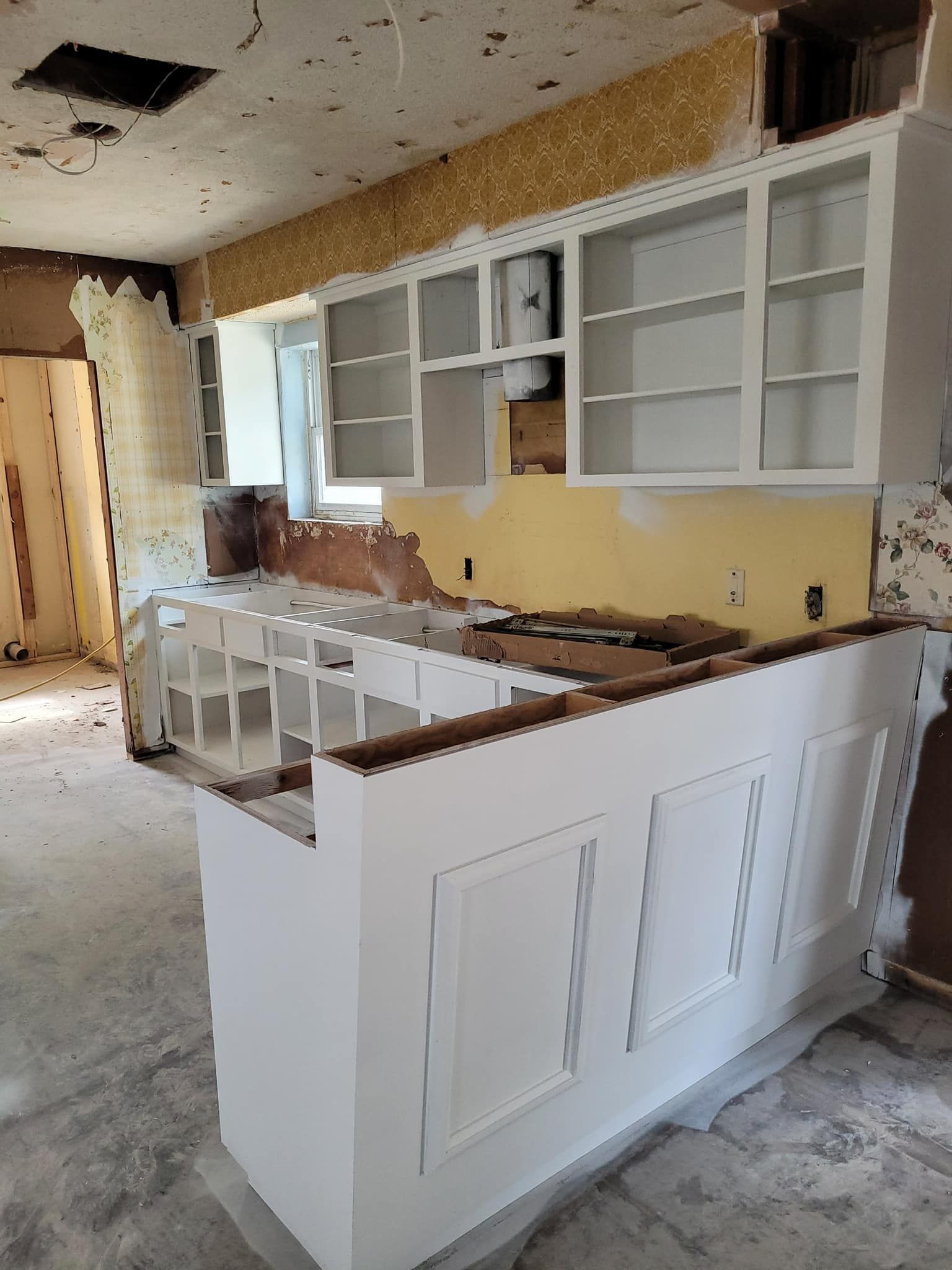 Damaged kitchen with torn cabinets, exposed wall, and debris on the floor during renovation