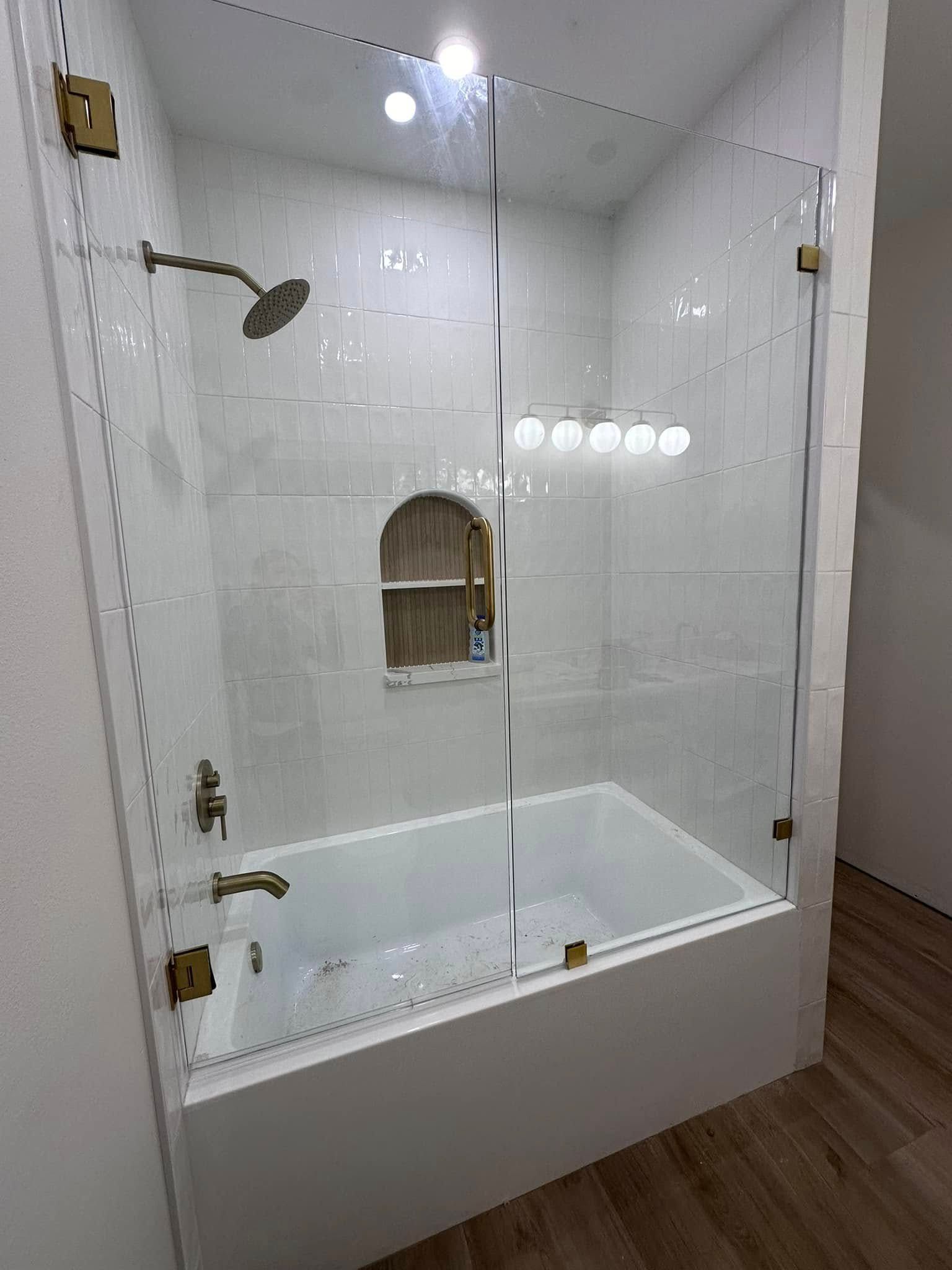 Empty white shower stall with glass doors, built-in shelf, and wood flooring outside