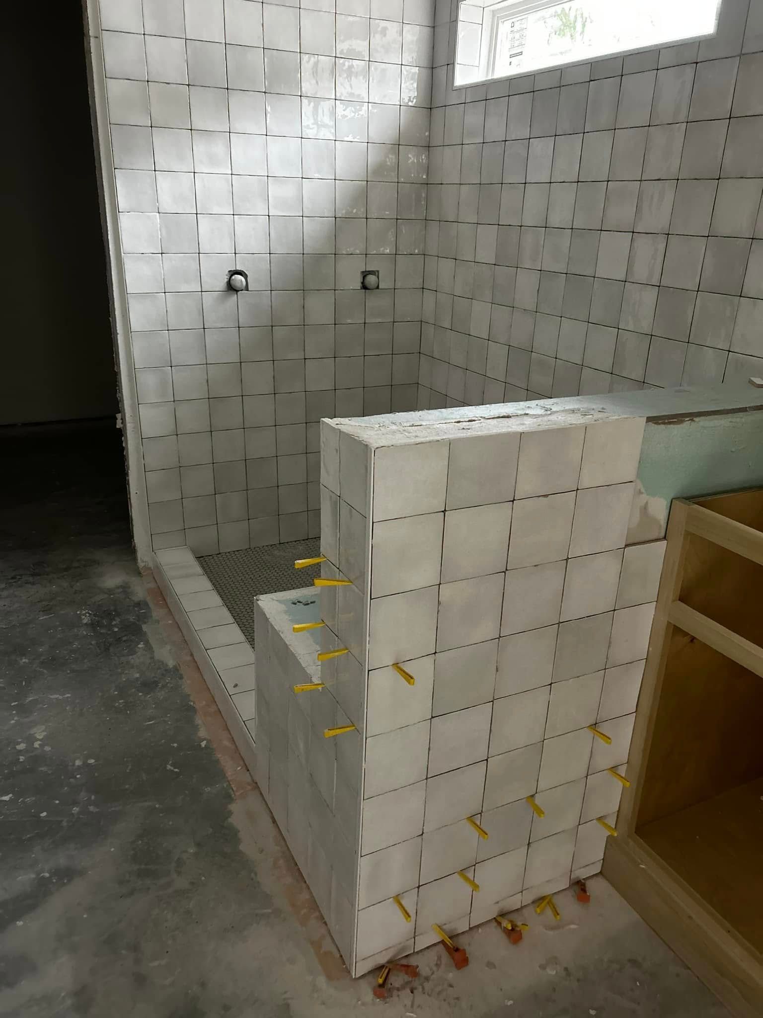 Stacked white tile boxes in a construction area beside a partially tiled wall and wooden cabinet.