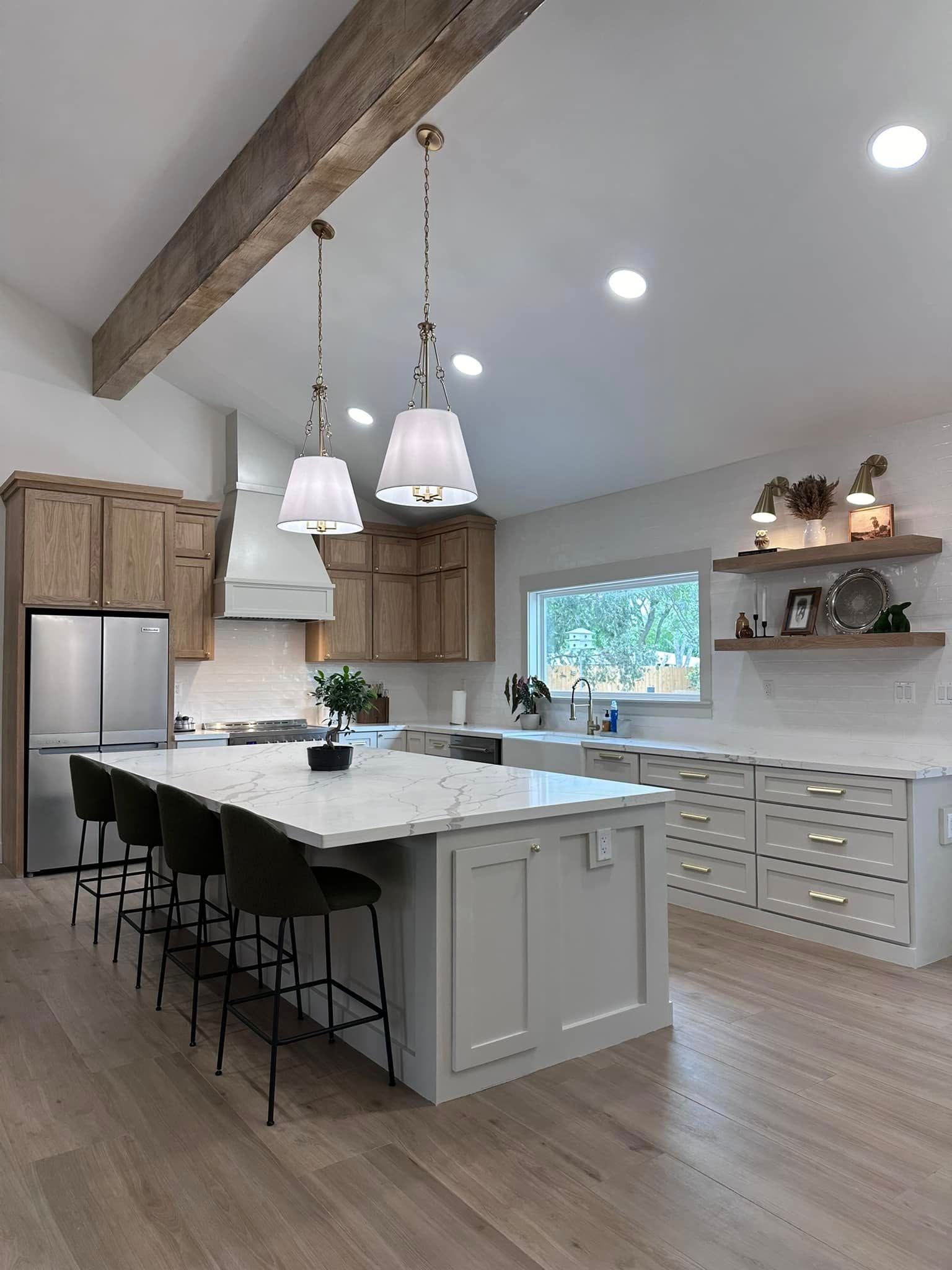 Bright modern kitchen with large white island, wood ceiling beam, bar stools, and pendant lights