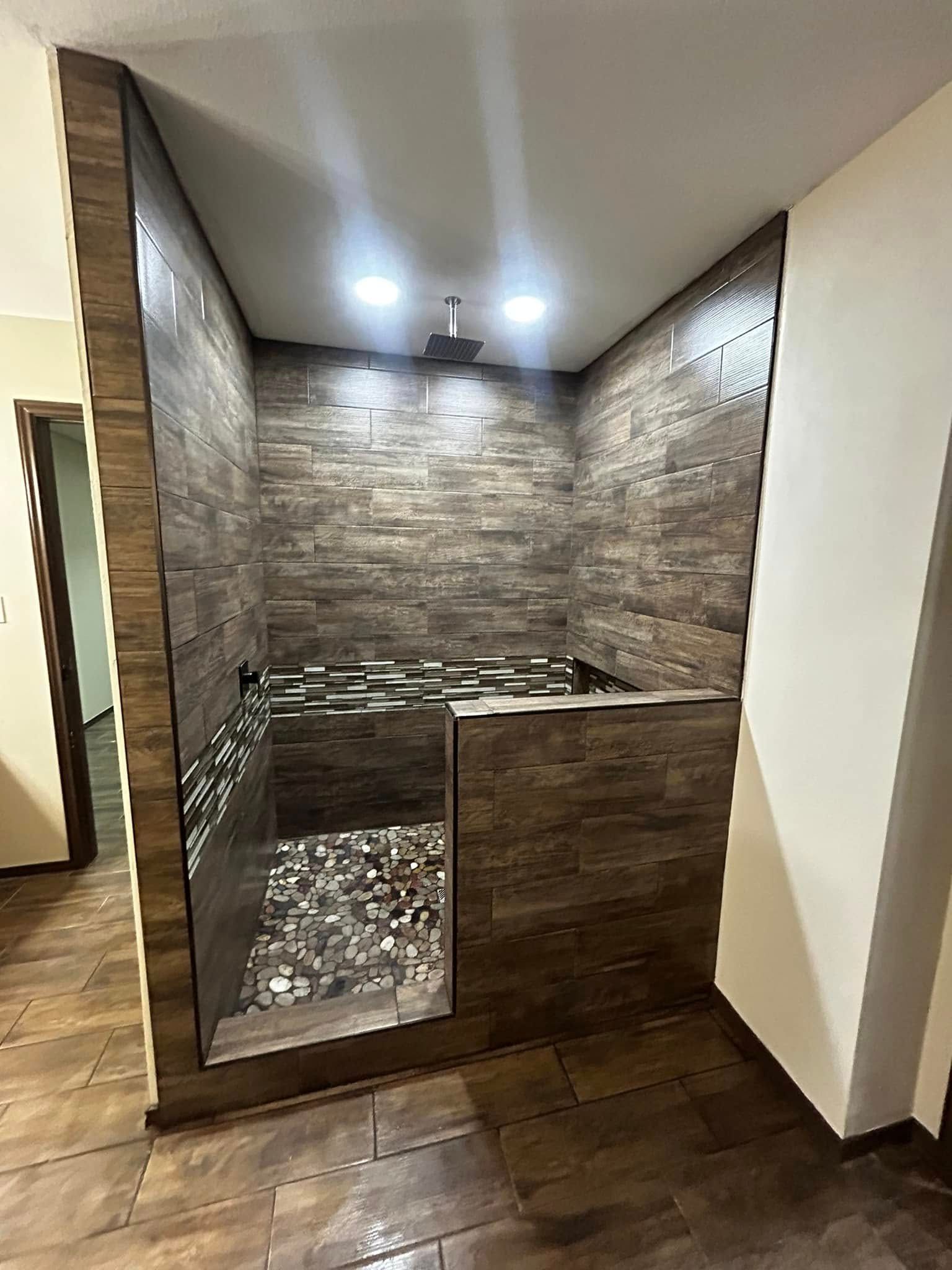 Small stone-tiled indoor shower or bath nook with a half-height wall and wood-look floor tiles.