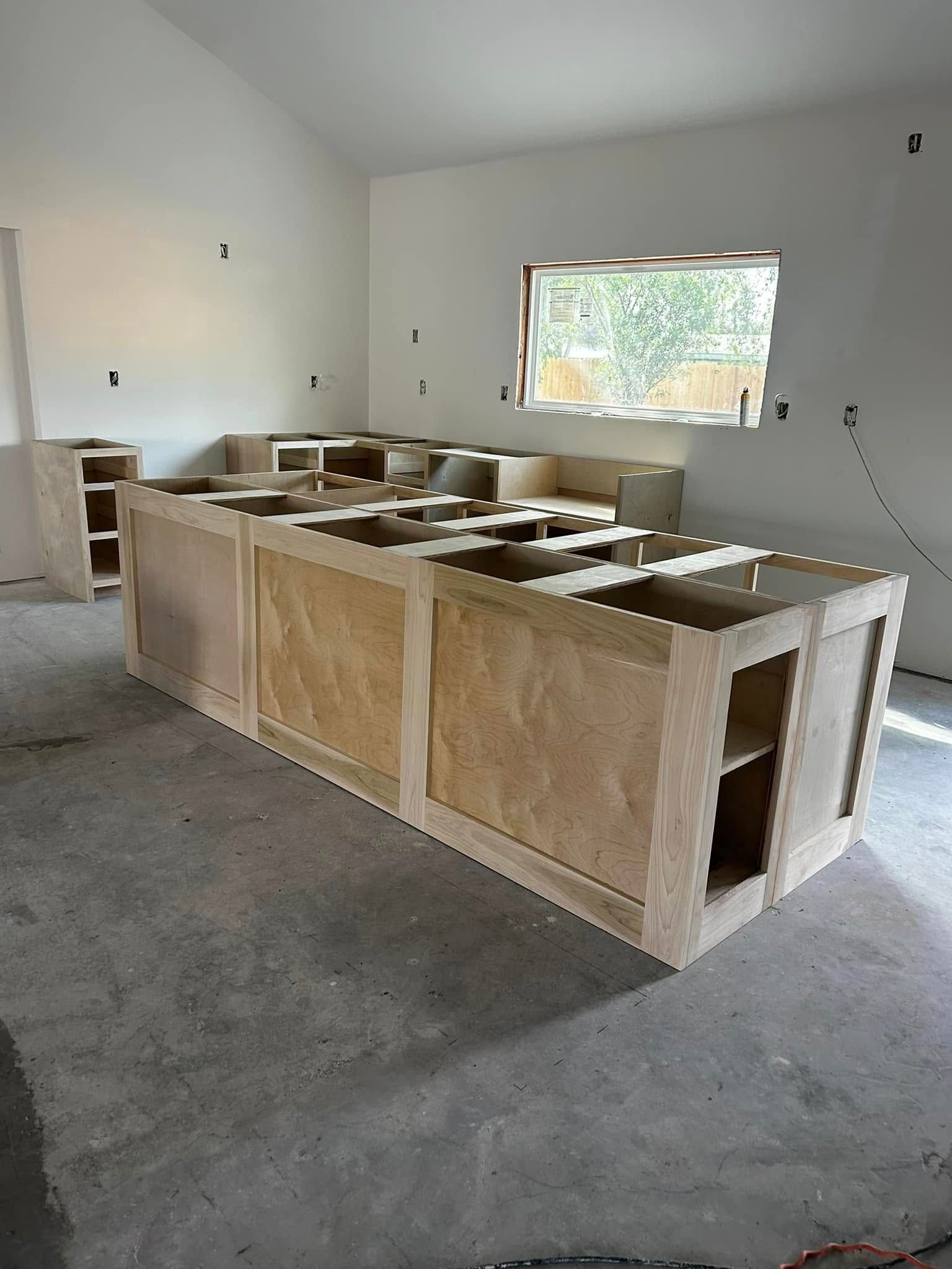 Unfinished kitchen with wooden cabinets and island in a white room, viewed from a concrete floor.