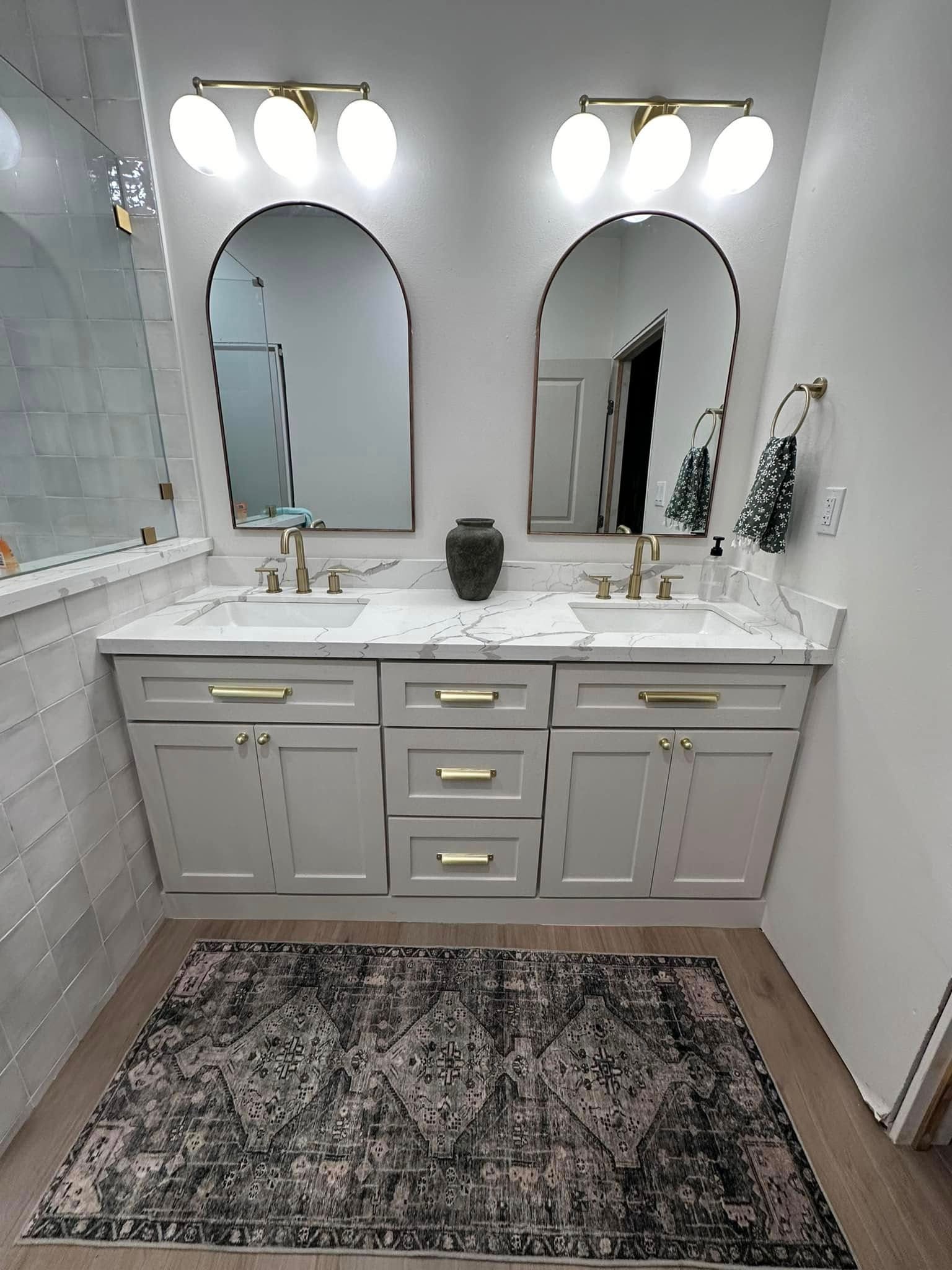 White bathroom vanity with double mirrors, brass fixtures, and patterned rug in a bright, modern bathroom