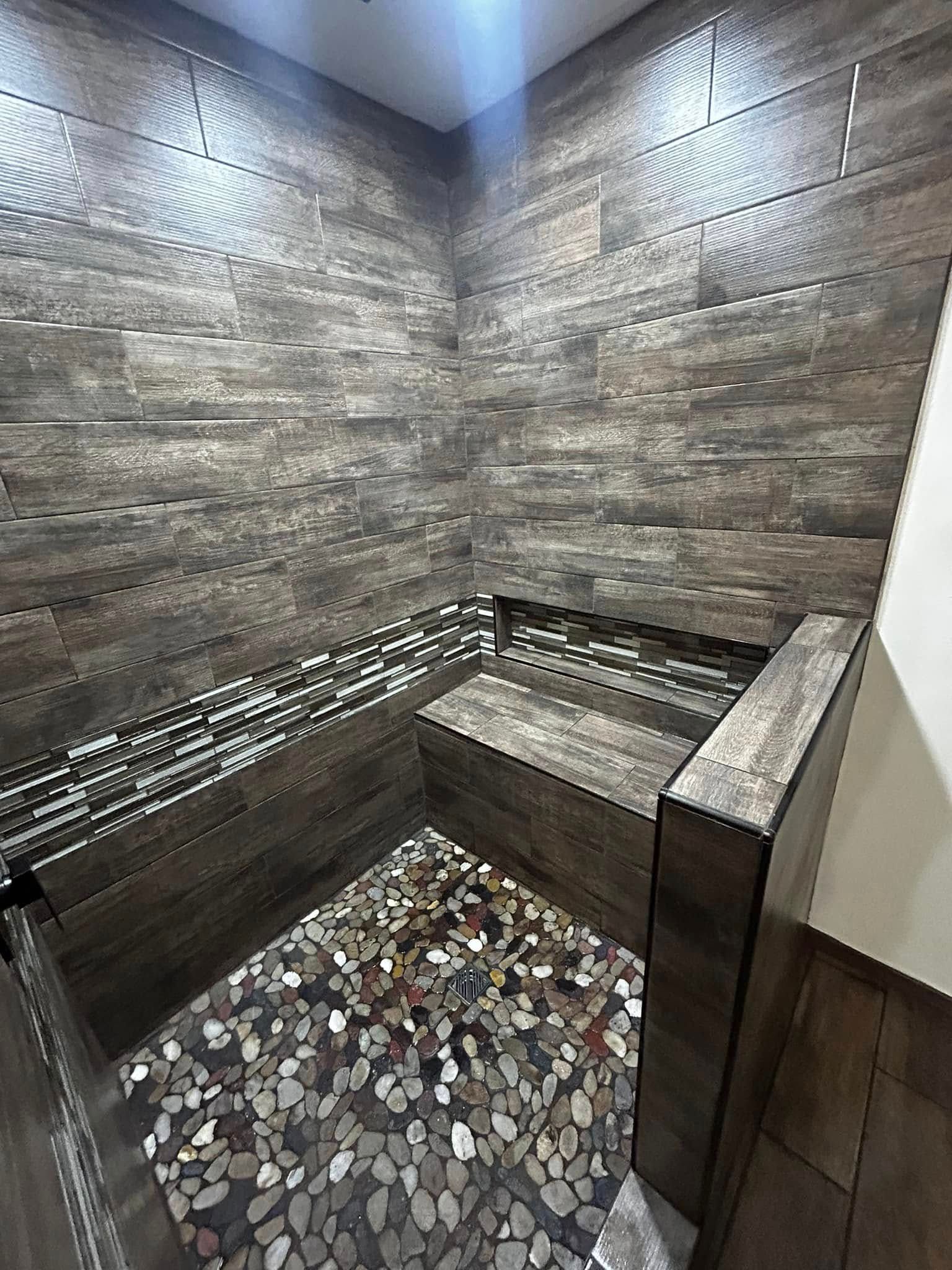 Modern tiled shower with stone walls, built-in bench, and pebble floor drain area