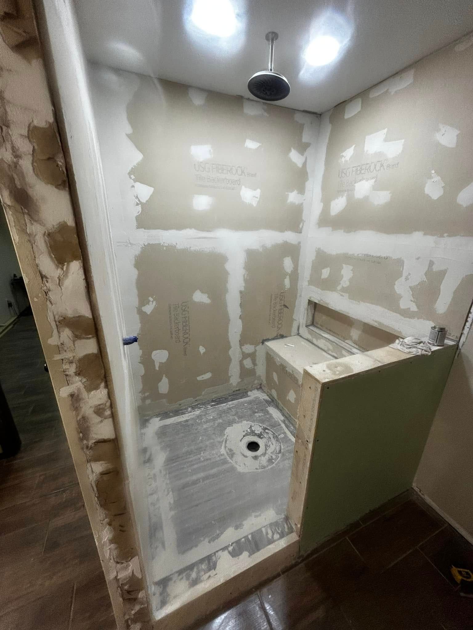 Small unfinished bathroom shower area with tiled floor, drywall patches, and a wall-mounted sink.