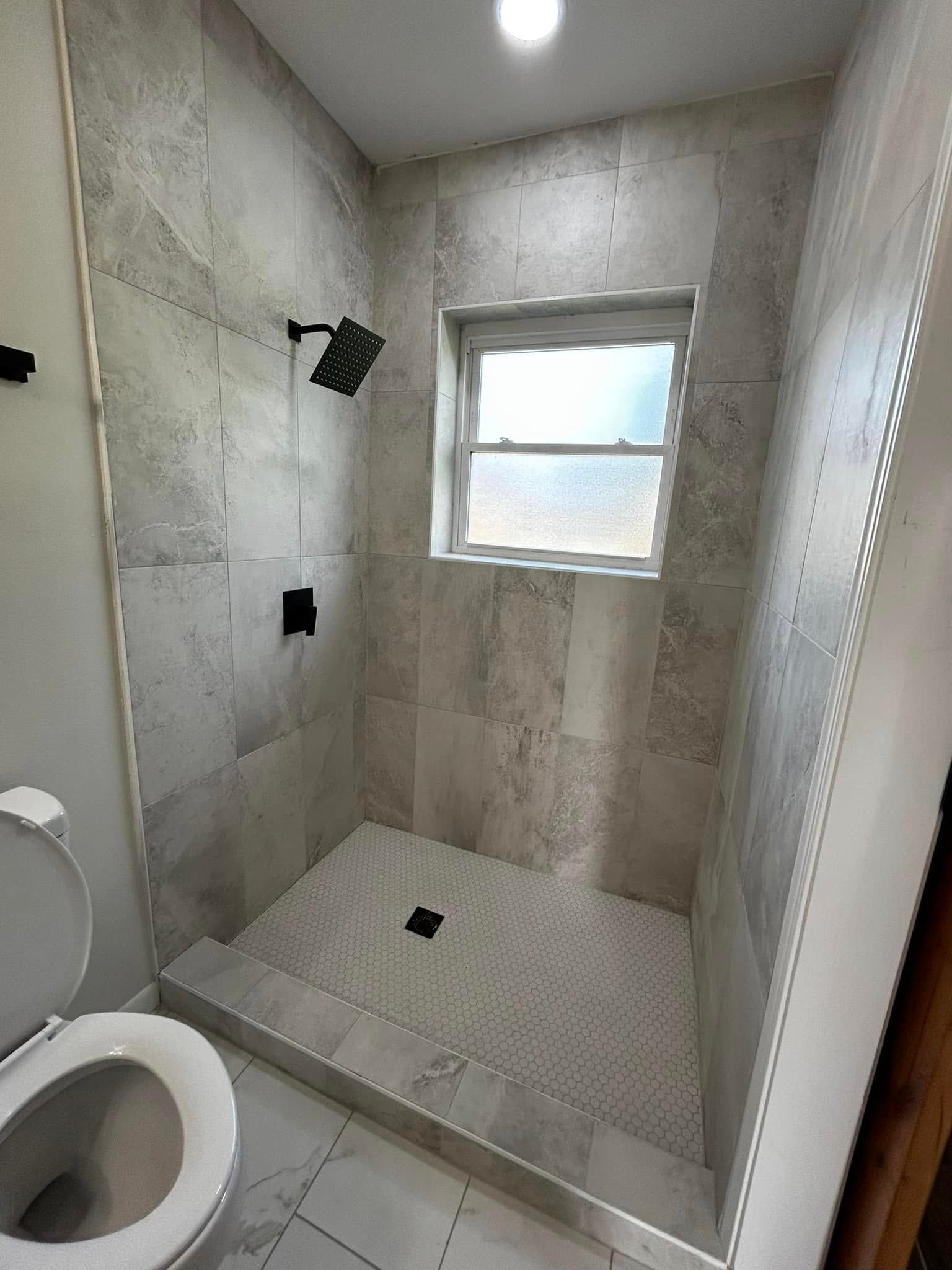 Small tiled bathroom with a walk-in shower, toilet, and frosted window.