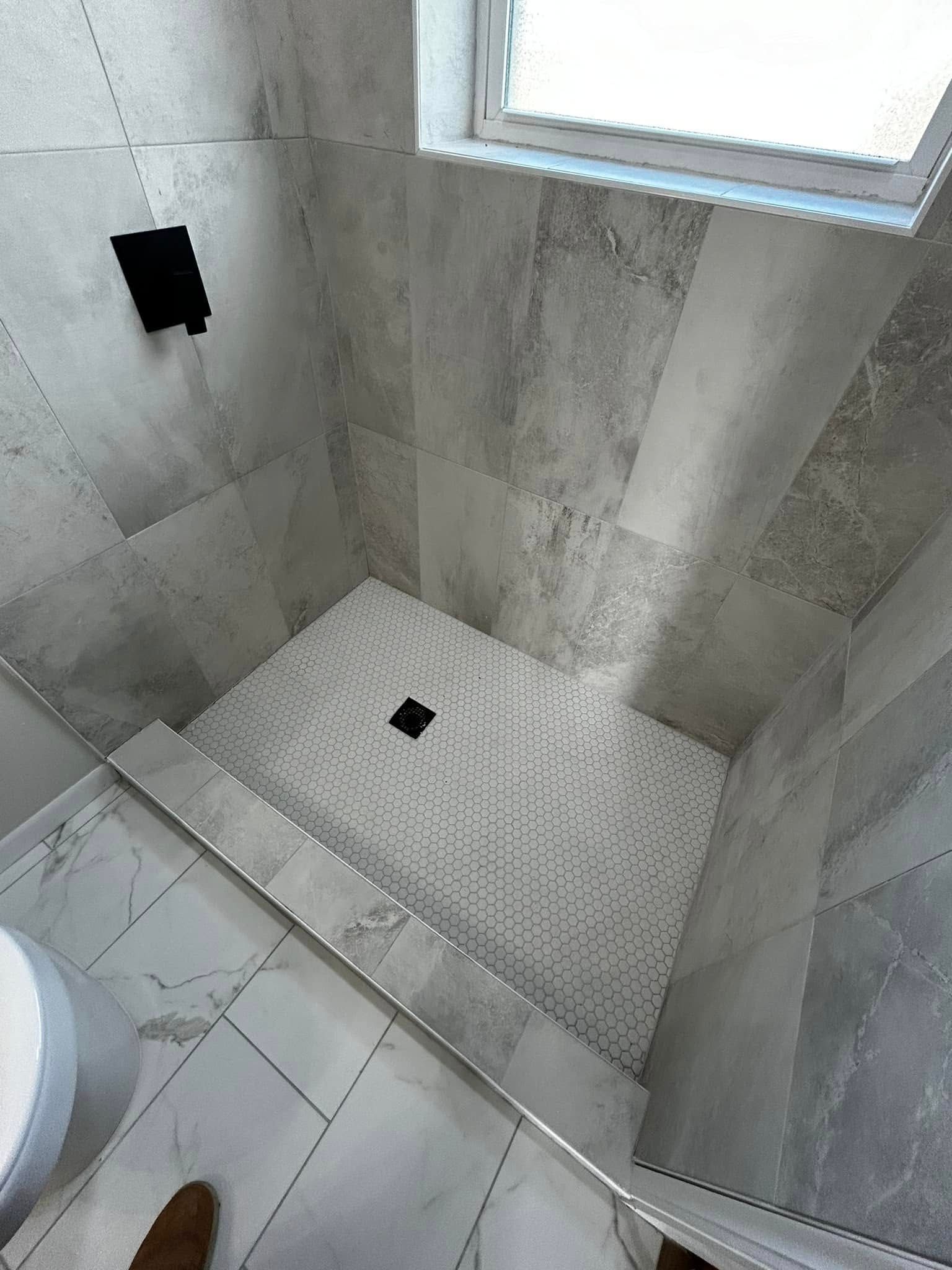 Small tiled shower with a built-in bench, floor drain, and gray stone walls.