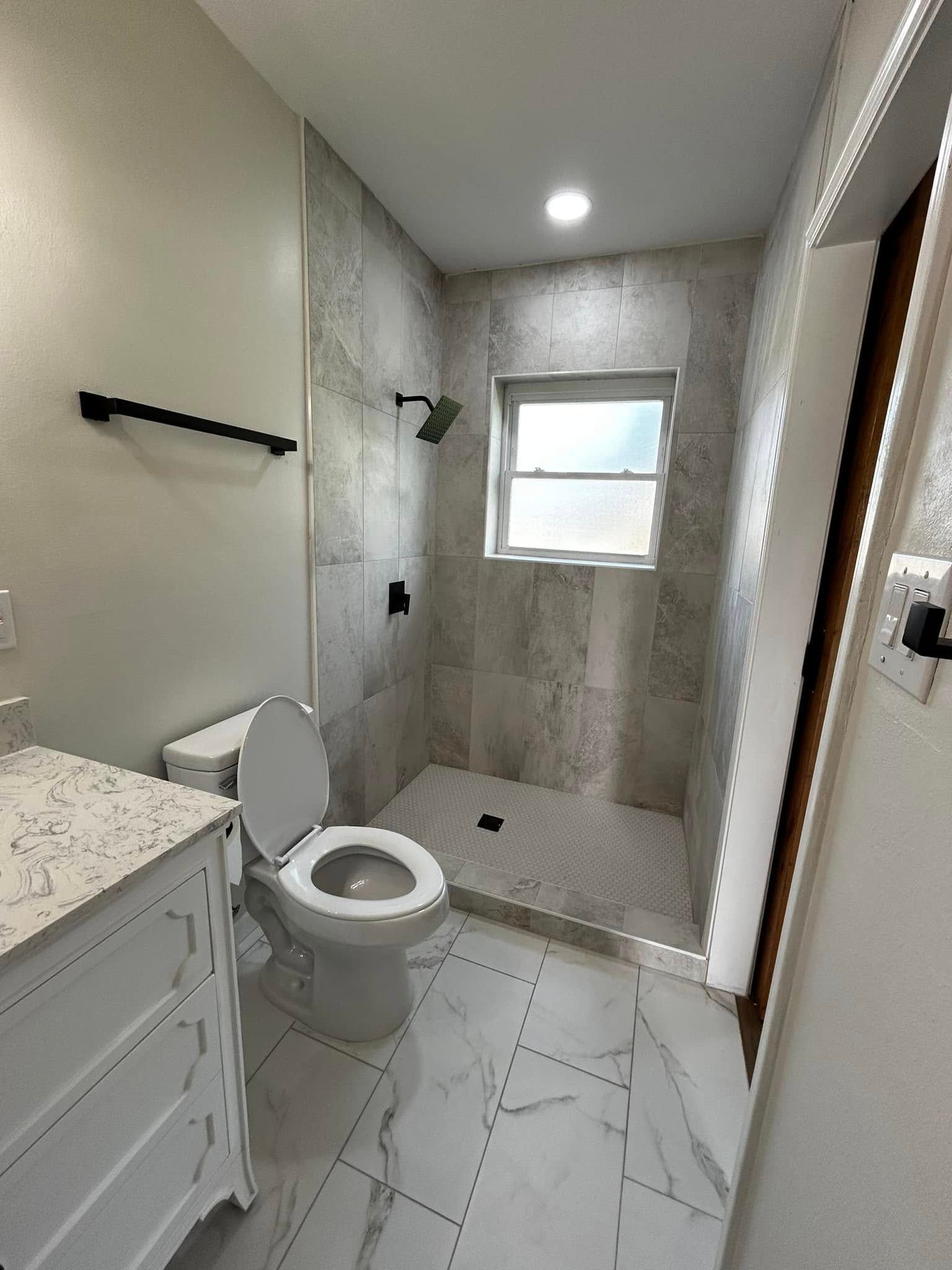 Compact bathroom with toilet, vanity, and tiled shower with window.