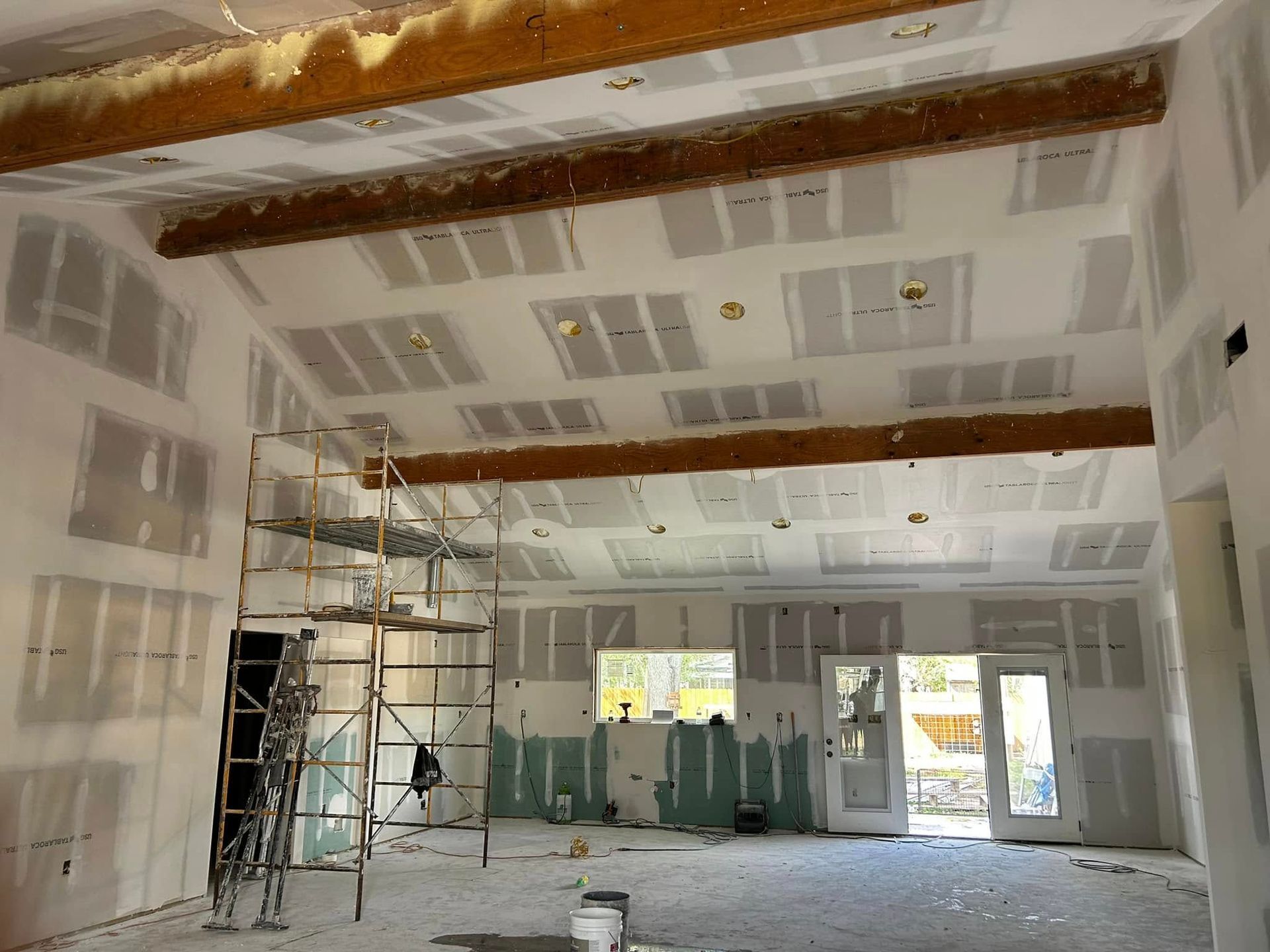 Interior of a drywall renovation with scaffolding, exposed ceiling beams, and unfinished walls.