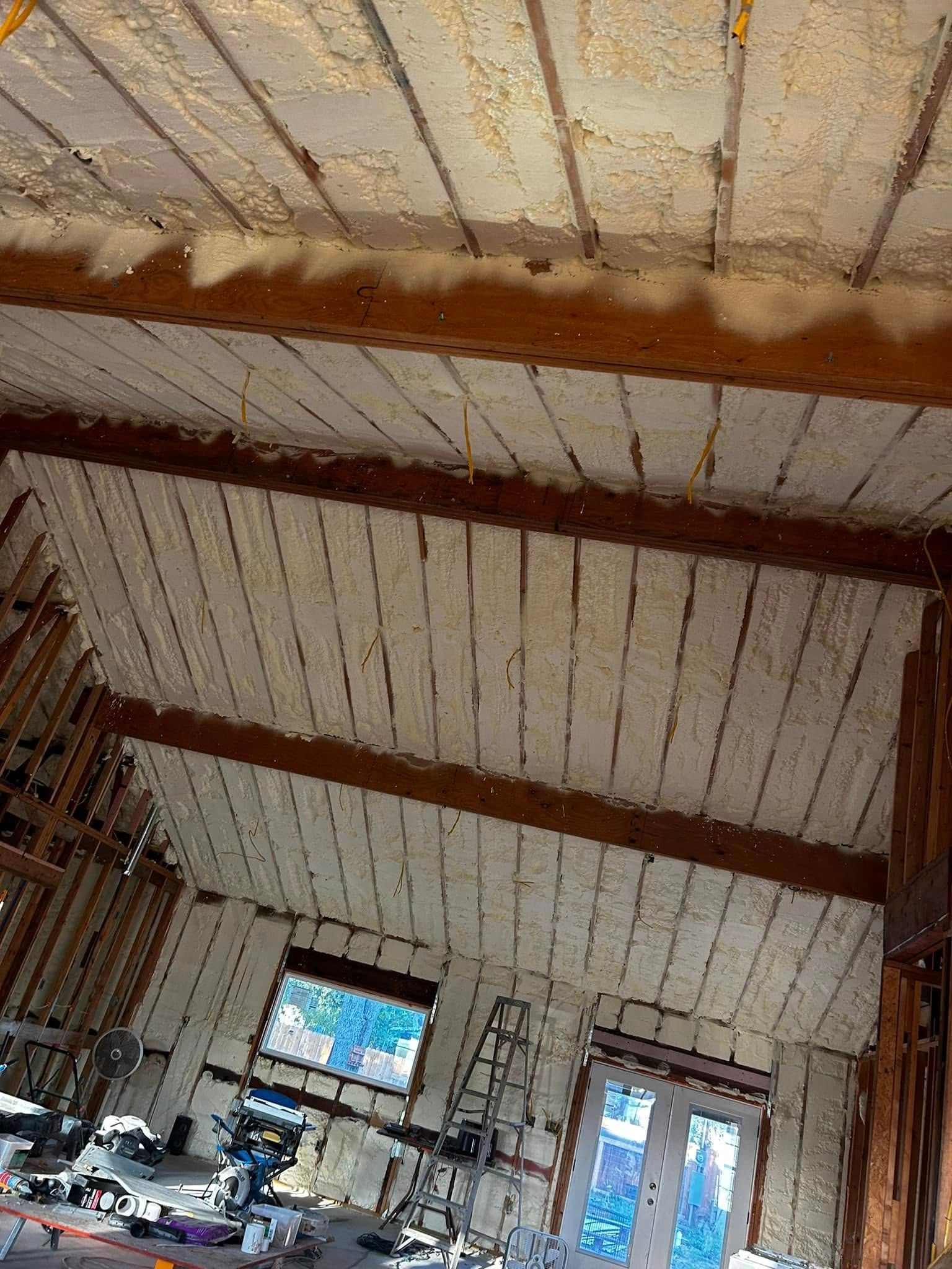 Interior of a rustic room with exposed beams, a TV, and a glass door letting in daylight