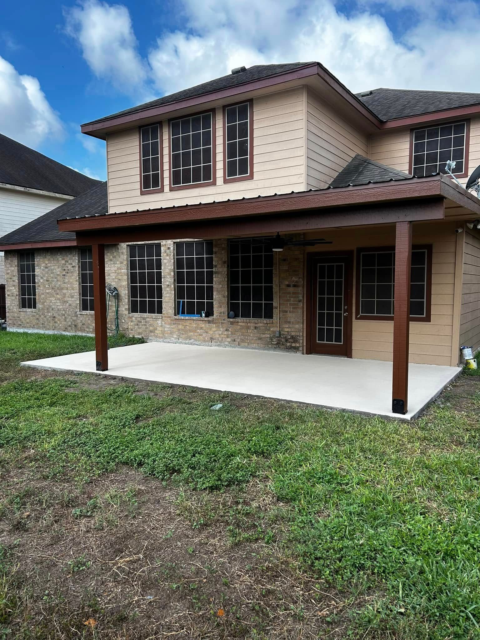 Two-story brick house with covered front porch, white columns, and small lawn under a blue sky