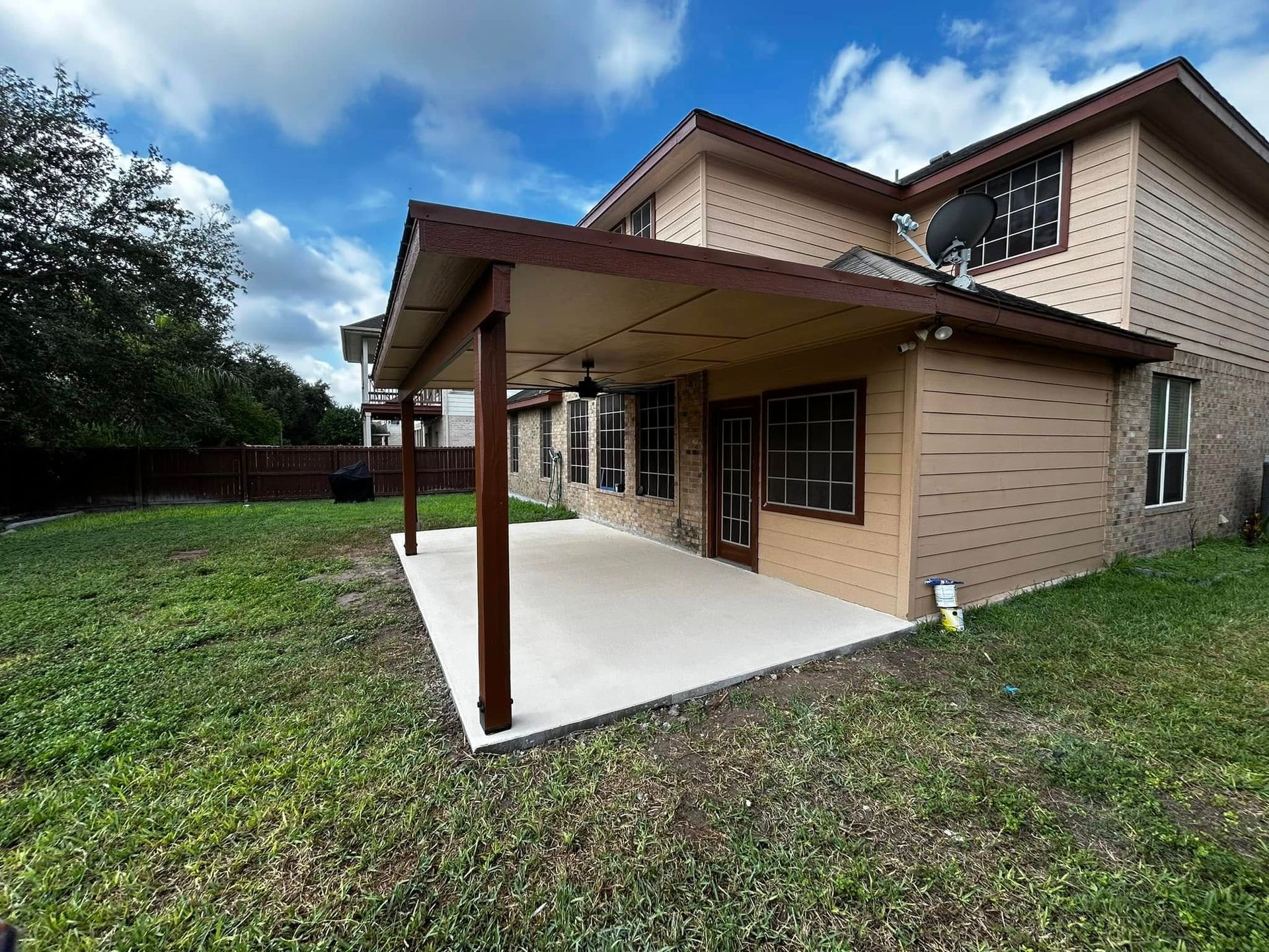Two-story tan brick house with a covered concrete patio and grassy yard
