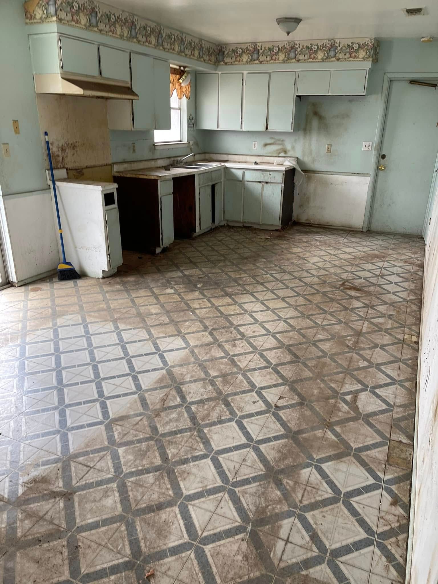An empty, outdated kitchen with worn cabinets, a patterned linoleum floor, and a small window.