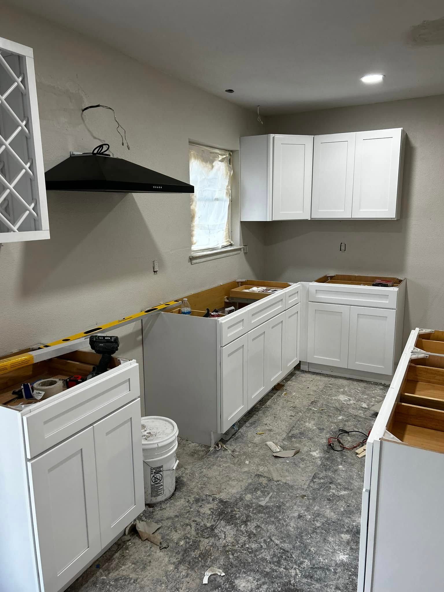 Unfinished kitchen with white cabinets, black range hood, and tools on the counters and floor