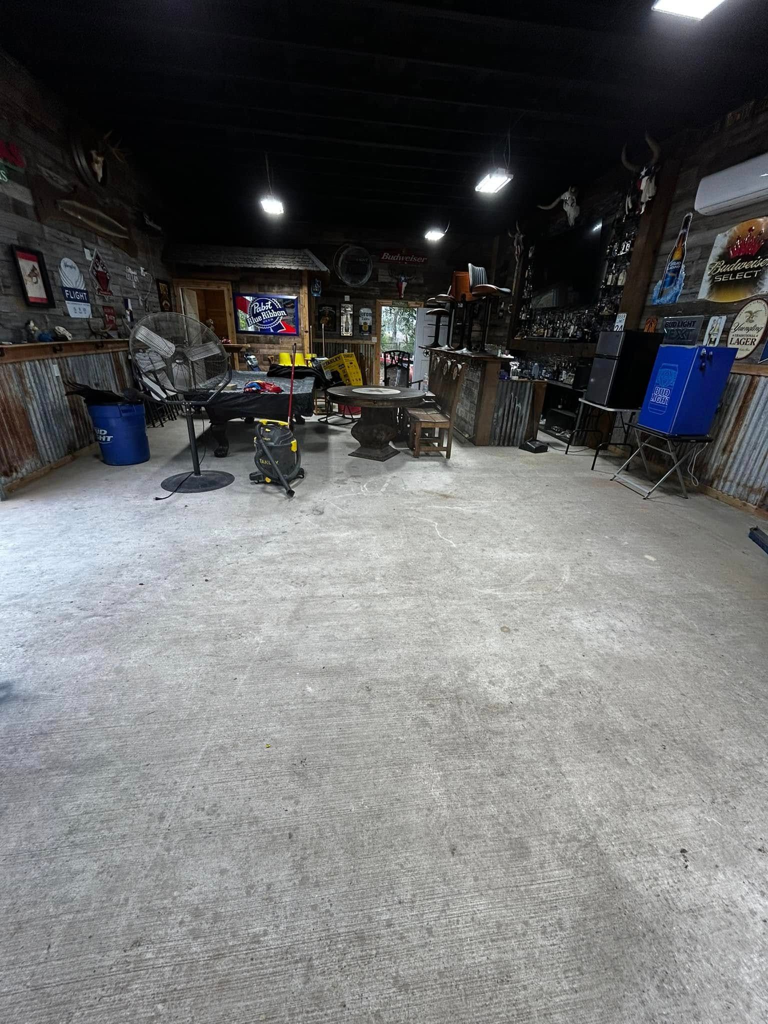 Wide view of a cluttered workshop or garage with tools, shelves, and chairs under dim ceiling lights