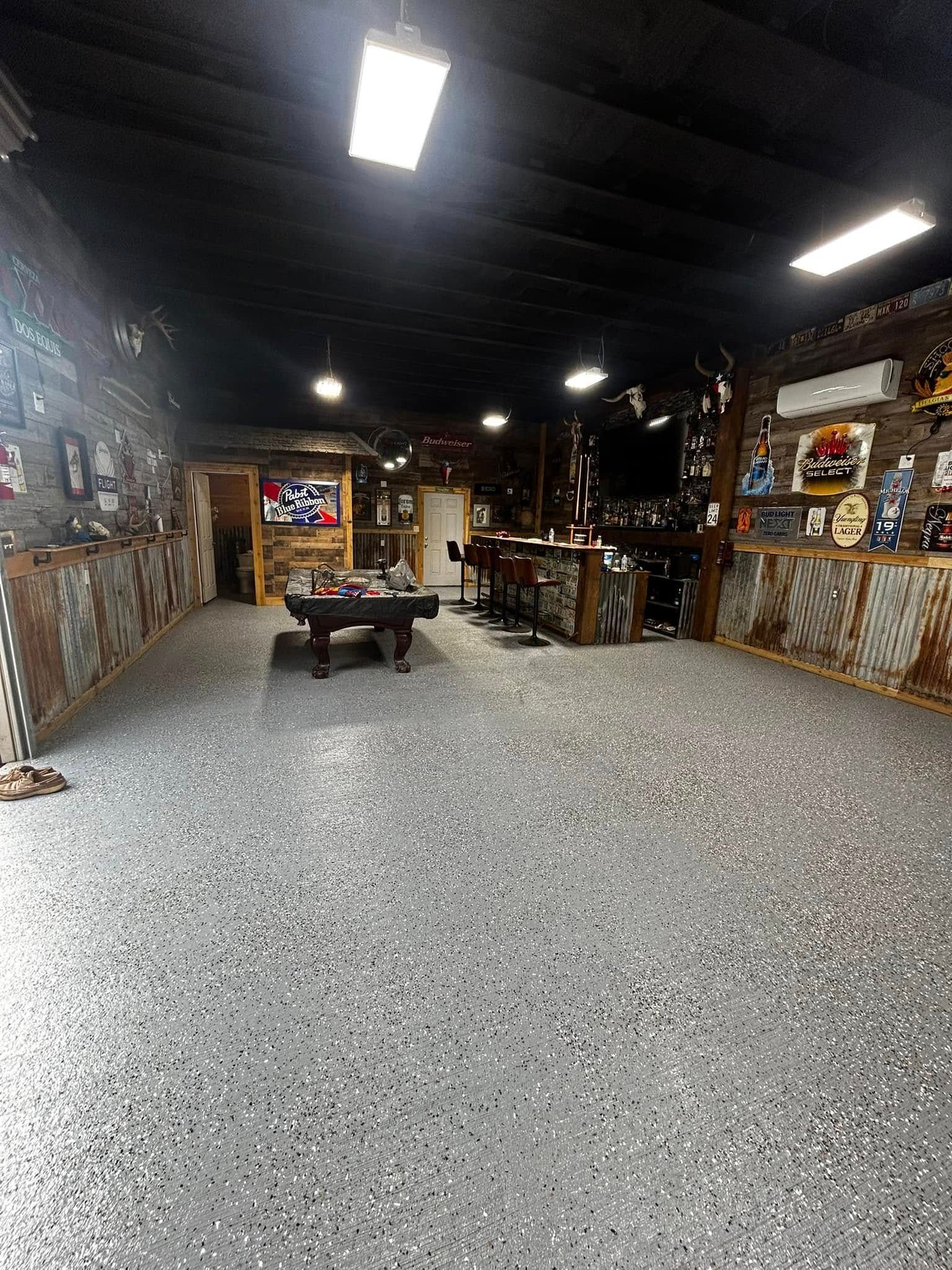 Indoor workshop or garage with speckled concrete floor, chalkboard wall, tables, and bright ceiling lights