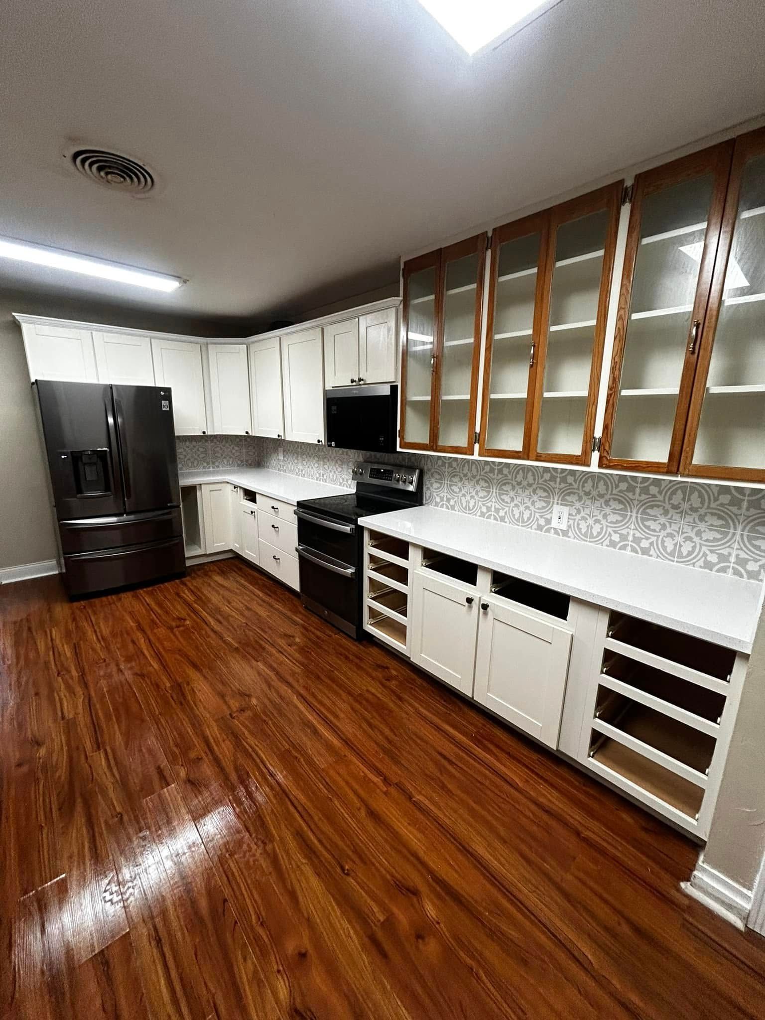 Bright kitchen with white cabinets, black appliances, wood floors, and a long countertop with upper windows