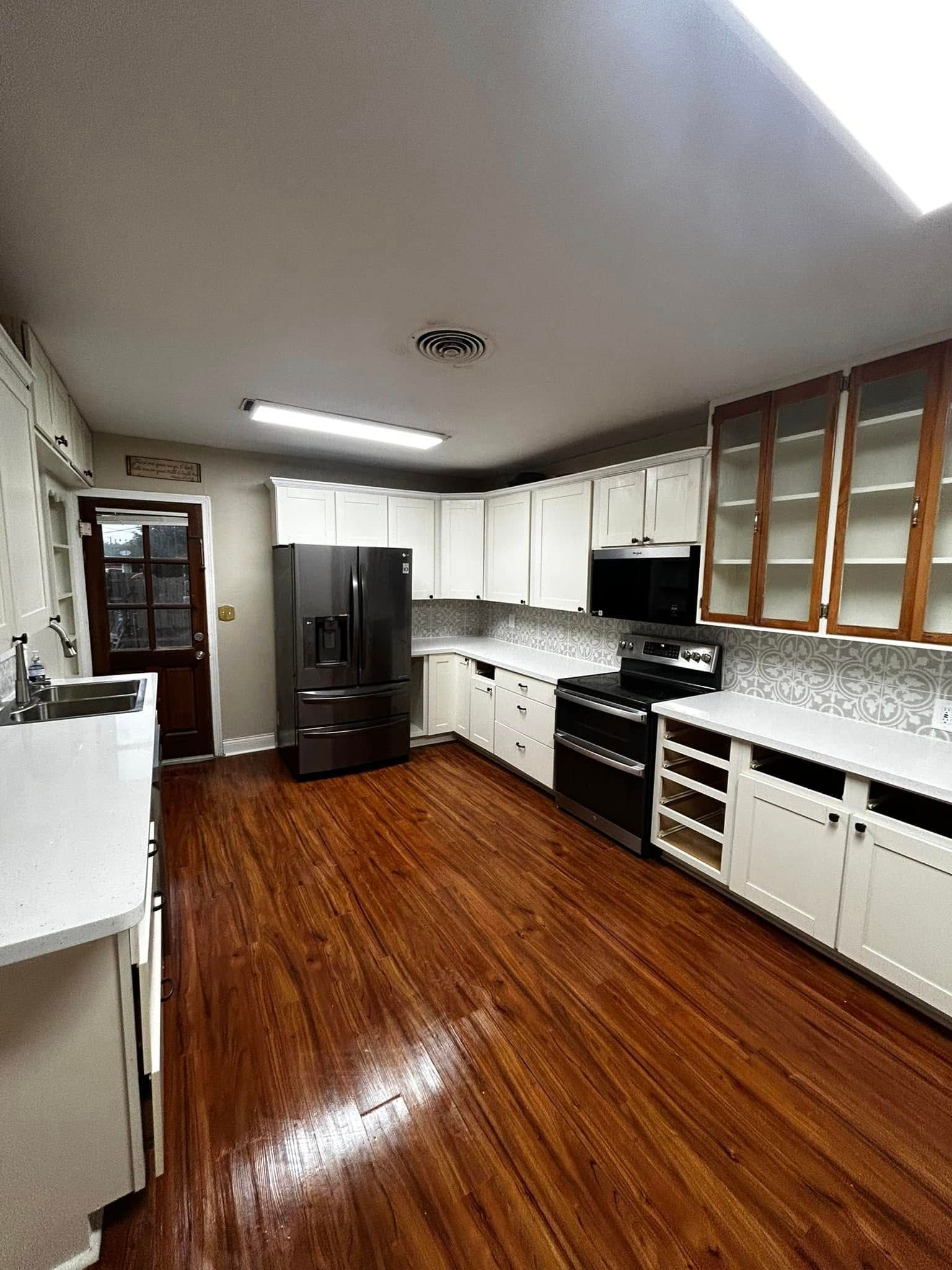 Empty kitchen with white cabinets, black appliances, and glossy wood floors beneath a sloped ceiling