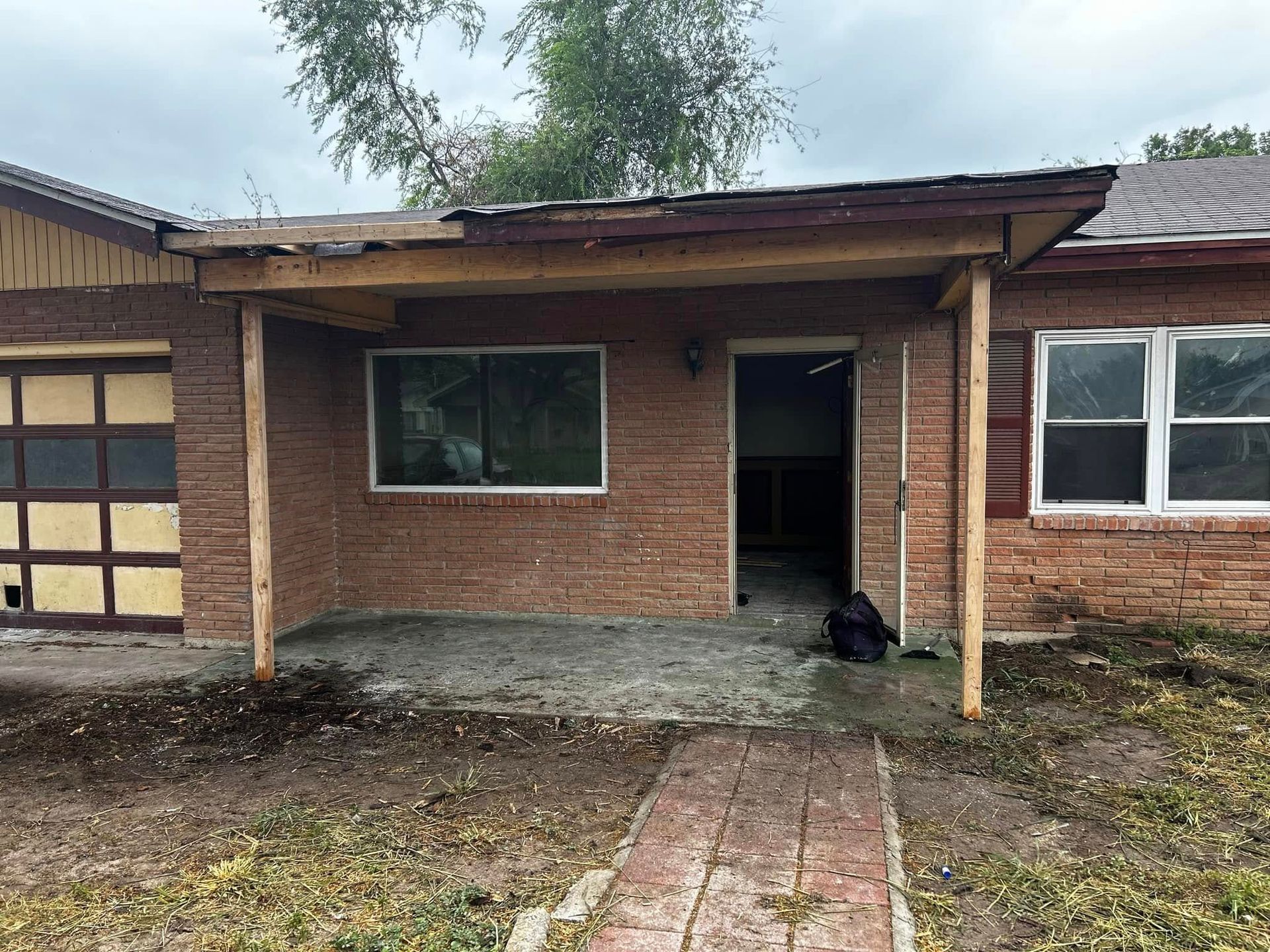 Damaged brick house entry with broken porch roof and muddy front yard