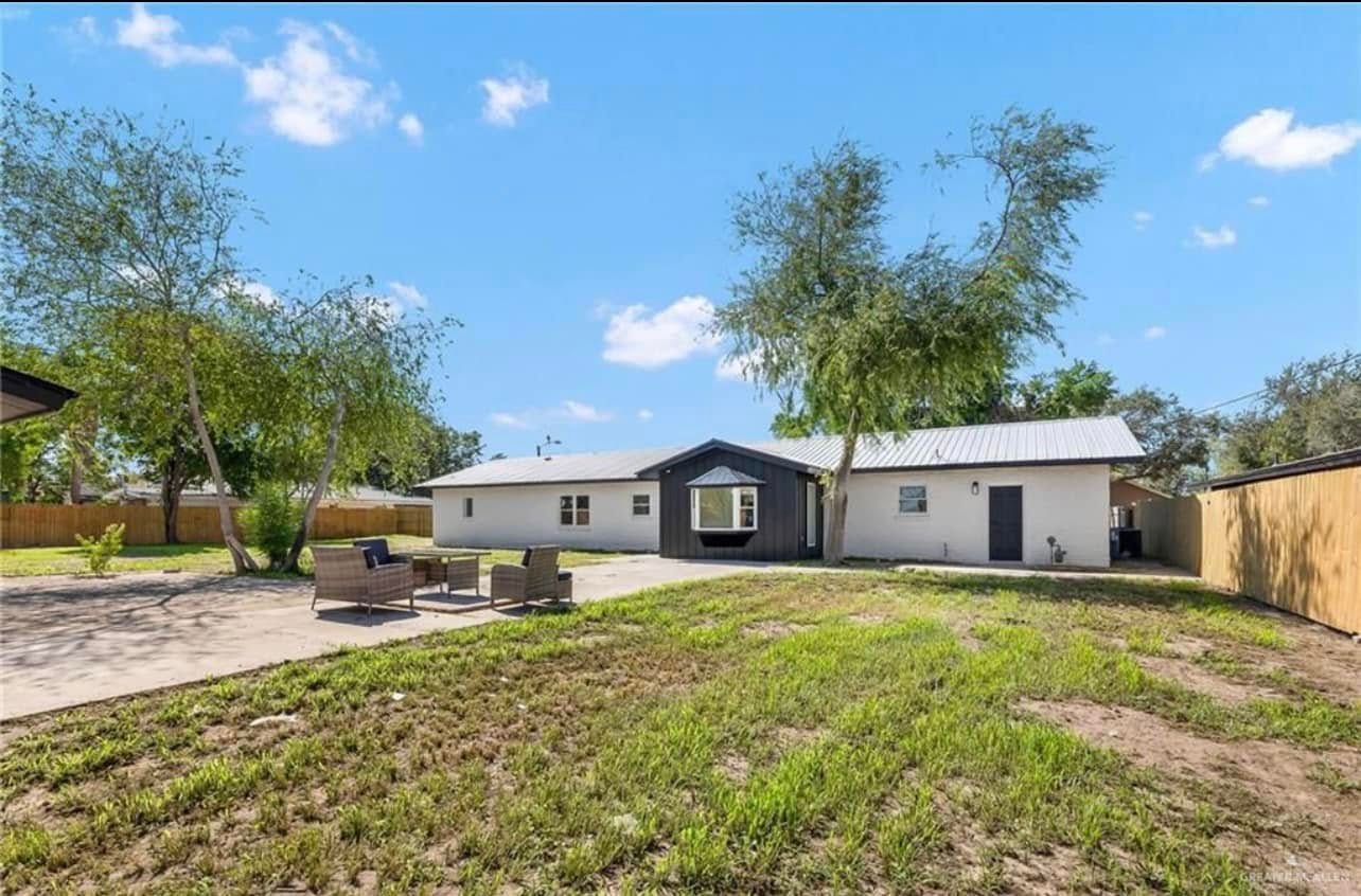 Single-story house with a large grassy yard, patio, and blue sky with trees.