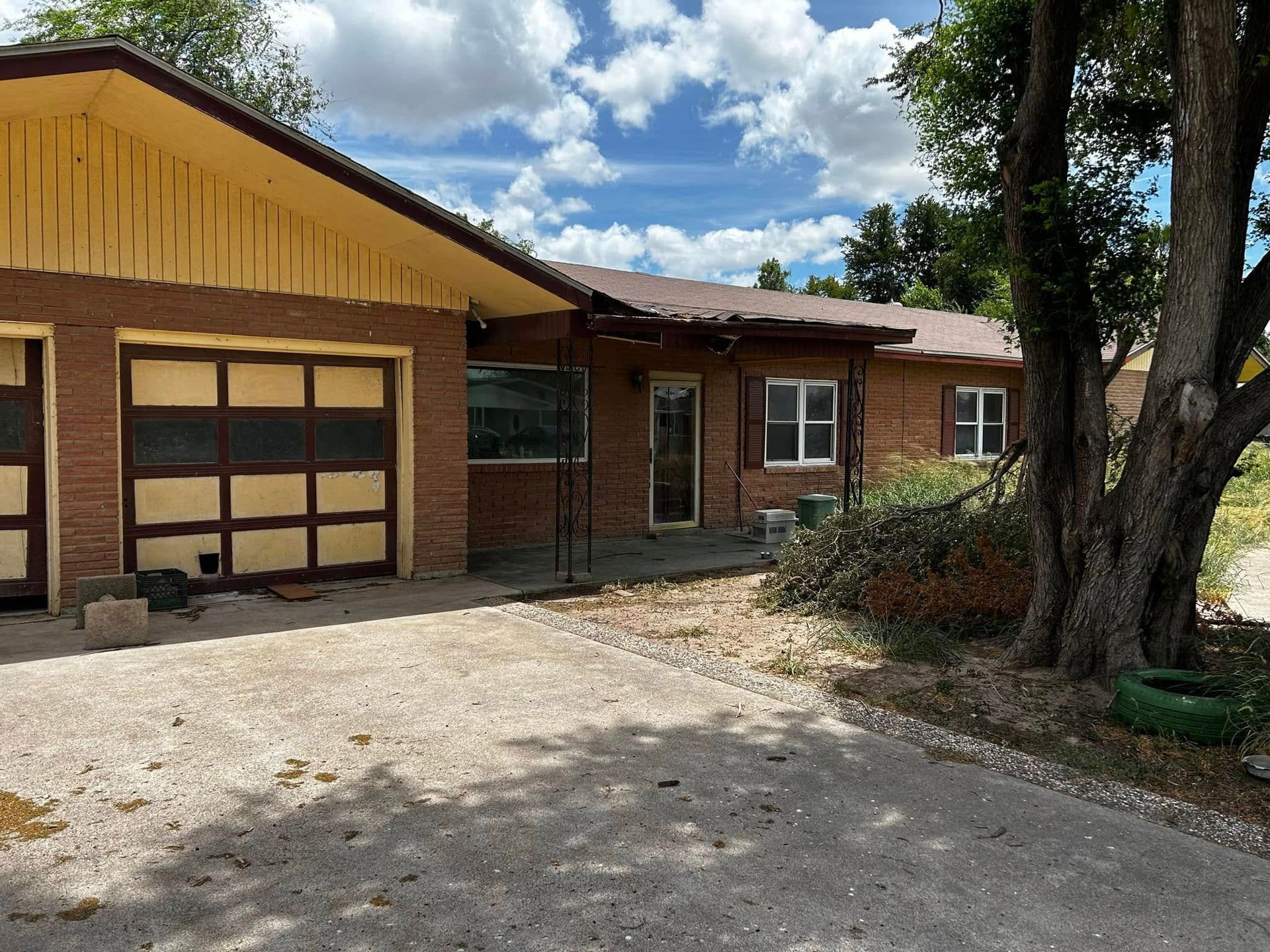 Single-story brick house with a garage, covered porch, and gravel driveway under a bright sky