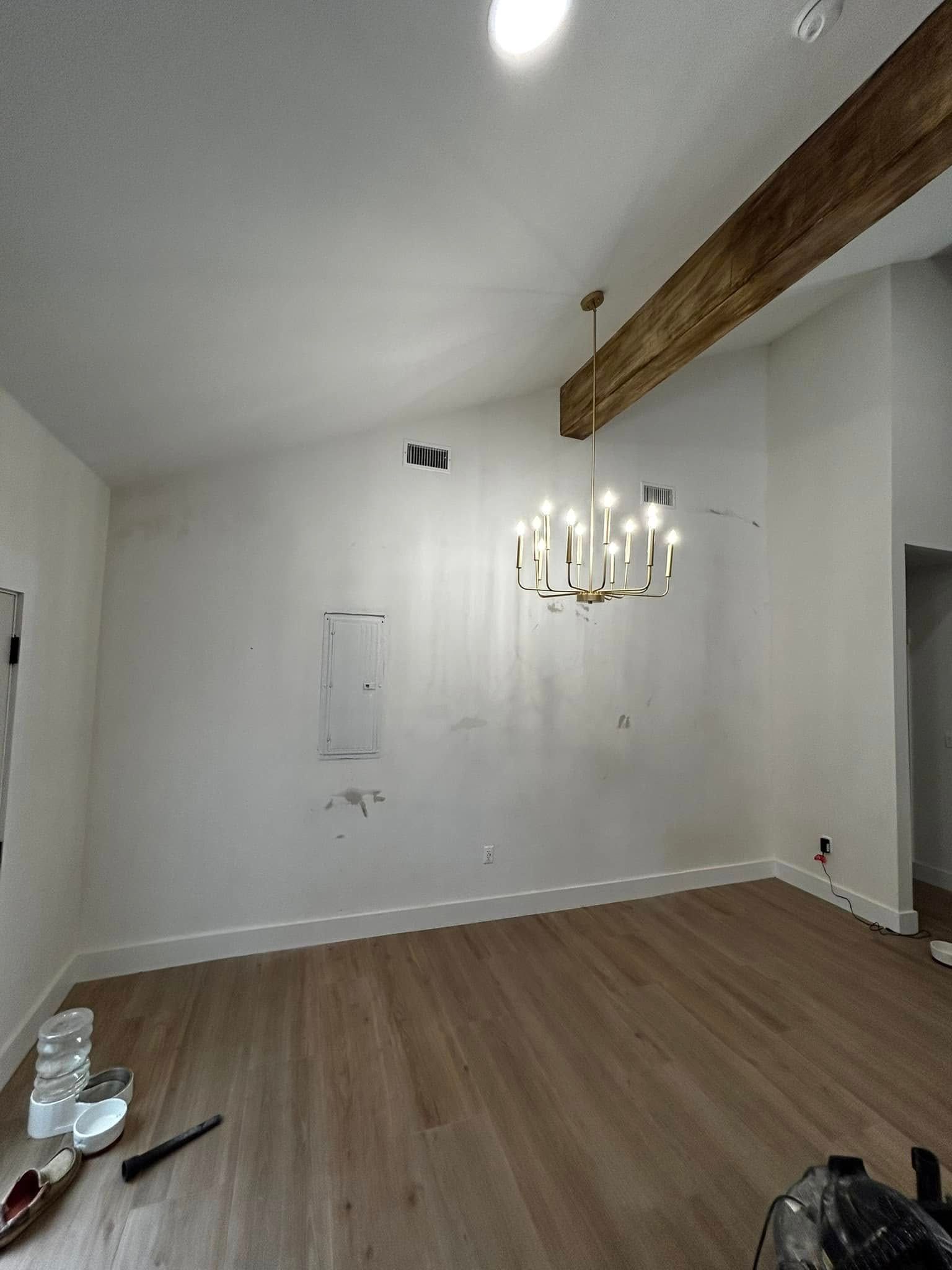 Empty white dining room with wood floor, exposed beam, and chandelier hanging from the ceiling.