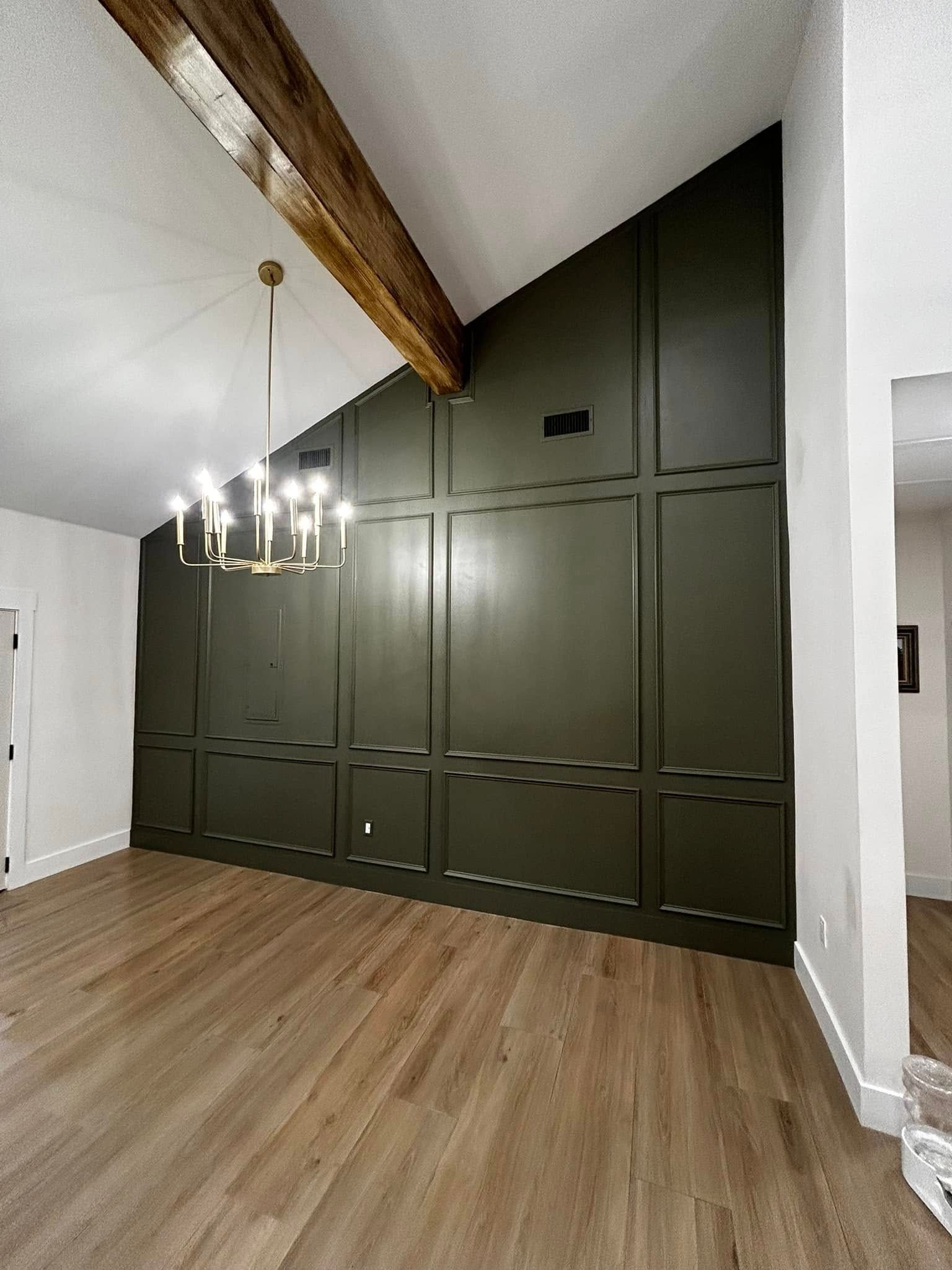 Empty modern living room with dark green built-in cabinets, exposed wood beam, and chandelier lighting