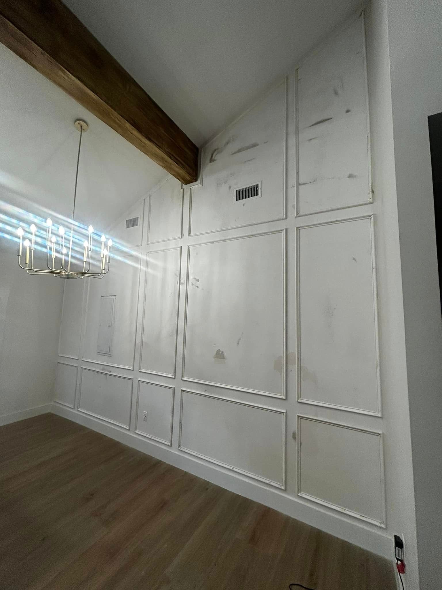 Empty white room with paneled walls, wood floor, exposed beam, and hanging closet rods