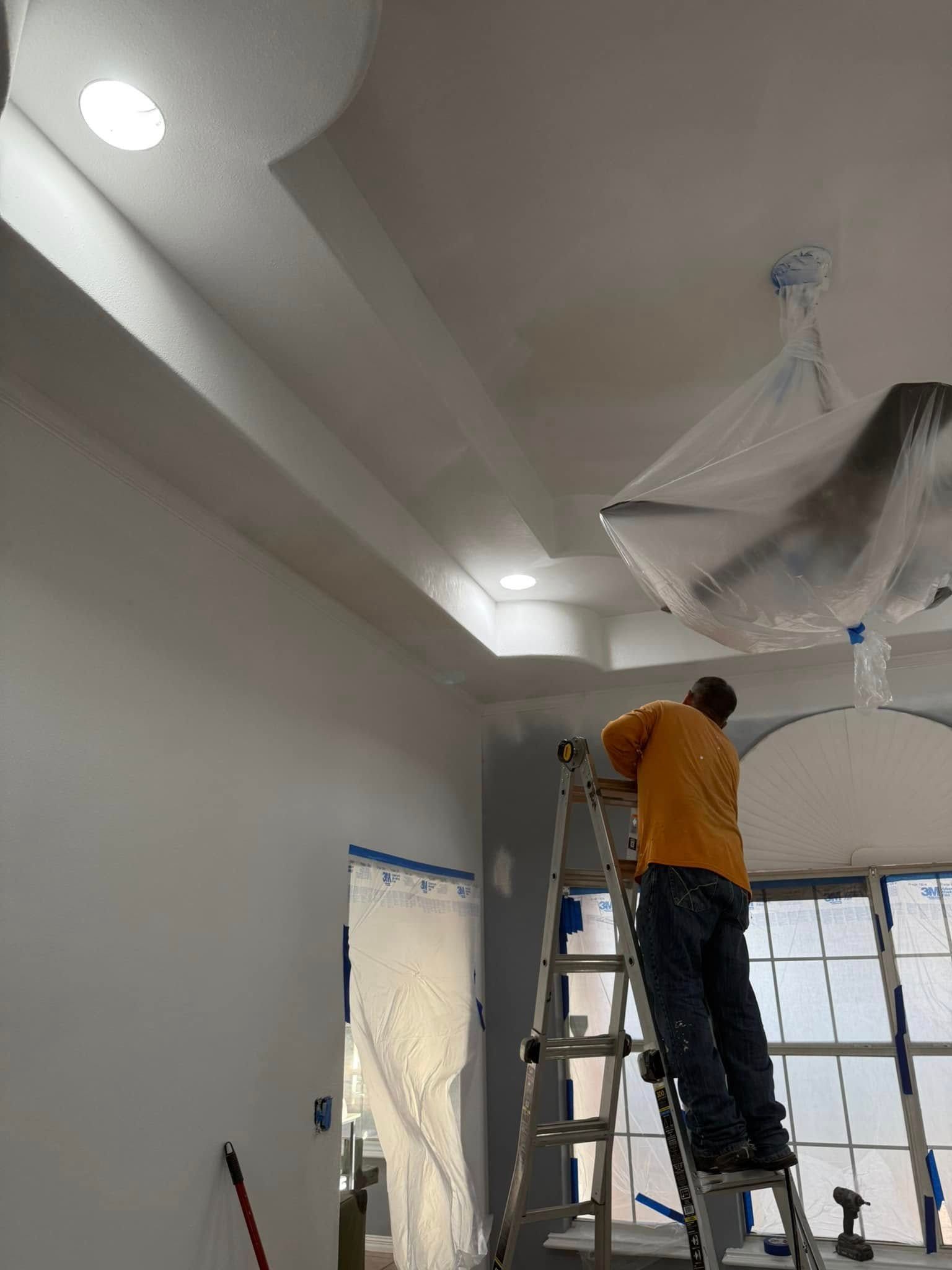 Worker on ladder installing ceiling fixture in a bright room with plastic-covered surfaces.