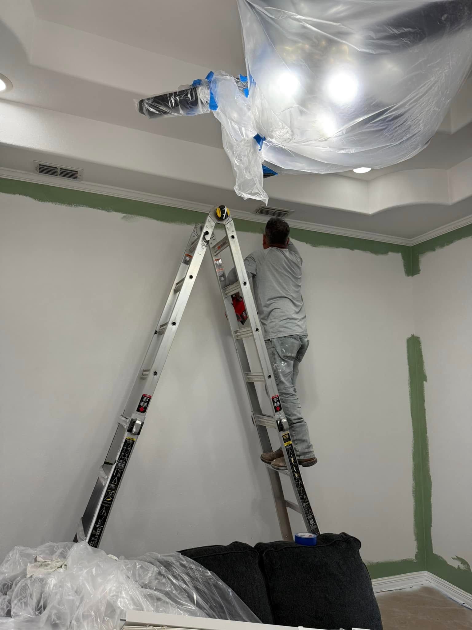 Person on ladder wrapping ceiling fixture in plastic during room painting or renovation